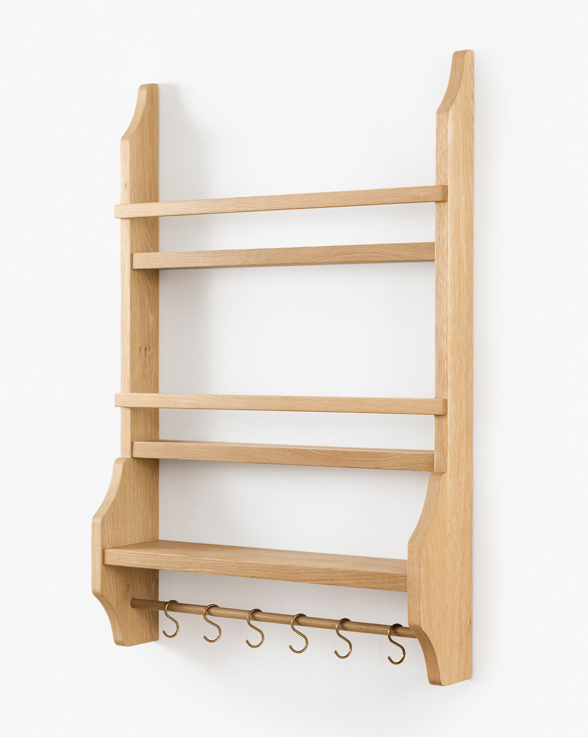 The Edna Kitchen Shelf is a wooden, wall-mounted unit with three open shelves, a lower ledge, and five metal hooks. Its heritage oak finish and angled side supports create timeless charm for your kitchen, by McGee & Co.