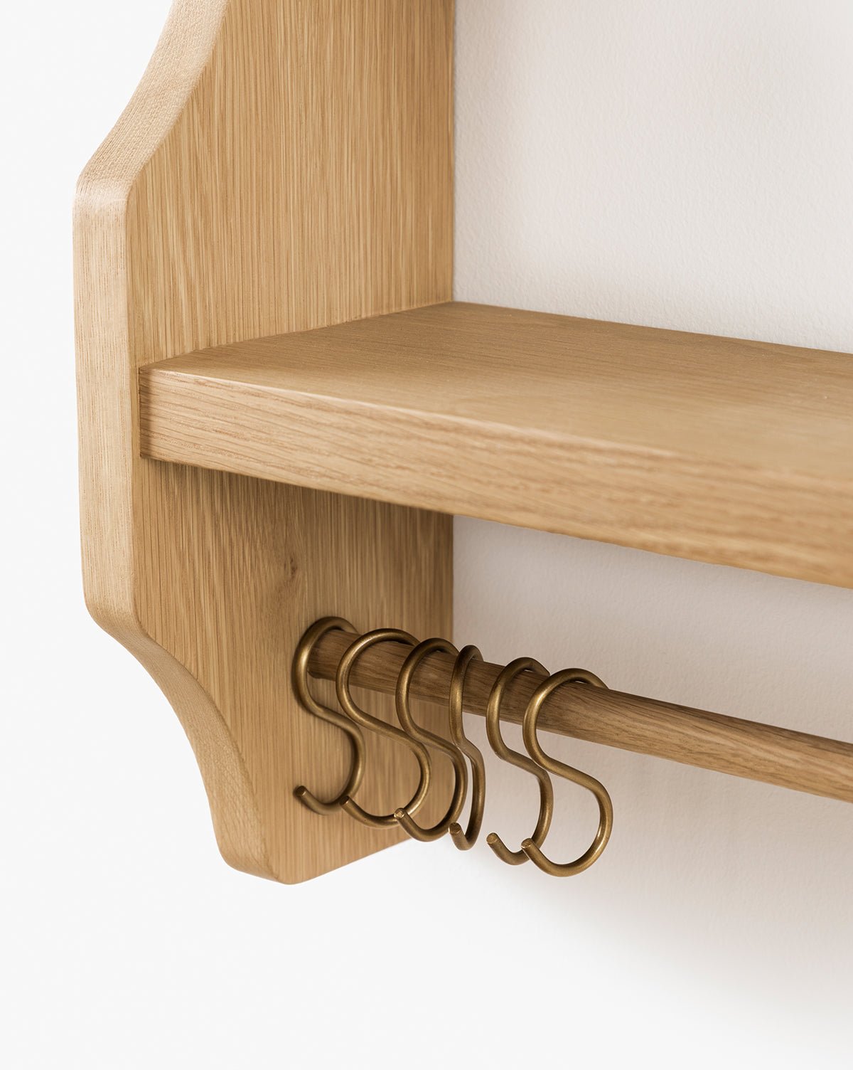 Close-up of the Edna Kitchen Shelf in heritage oak with a smooth finish, featuring a horizontal rod and brass S-hooks. This open shelving unit is mounted on a white wall, by McGee & Co.