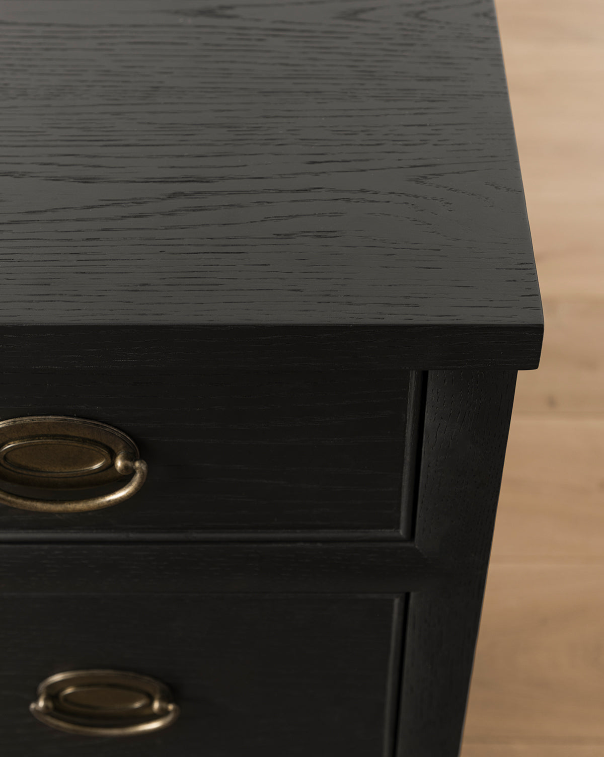 Close-up of the Edward Dresser in Black Ash with brass oval handles, showing visible wood grain on the surface and drawers. Ideal for bedroom storage, it is pictured standing on a light wood floor, by McGee & Co.