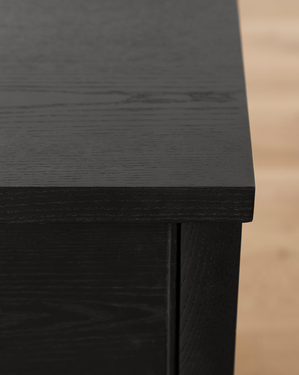 Close-up of the corner of the Edward Nightstand in Black Ash, highlighting its smooth surface and straight edges with a blurred light wood floor in the background, by McGee & Co.