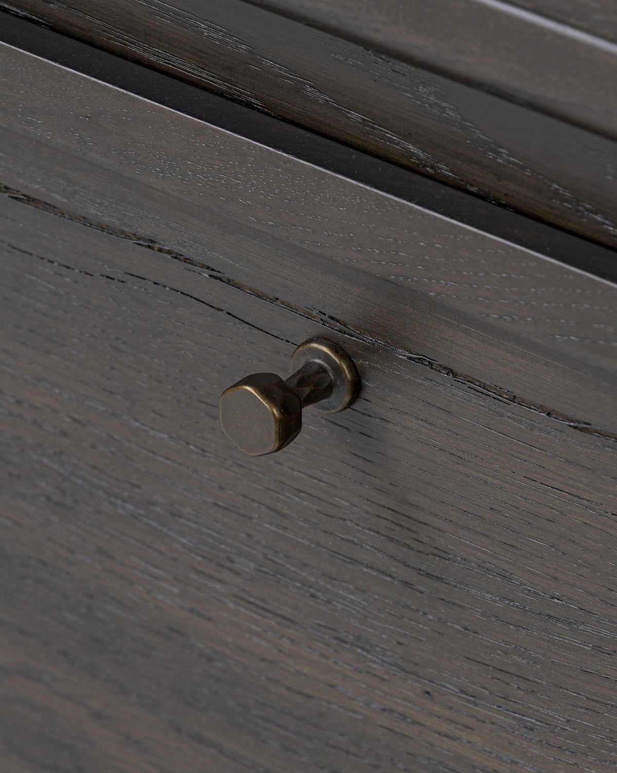 Close-up of the Eldoria Oak Sideboard drawer front, featuring dark wood grain and a small round antique brass knob. Its textured finish enhances the rustic charm and modern deco style of this elegant furniture piece, by McGee & Co.