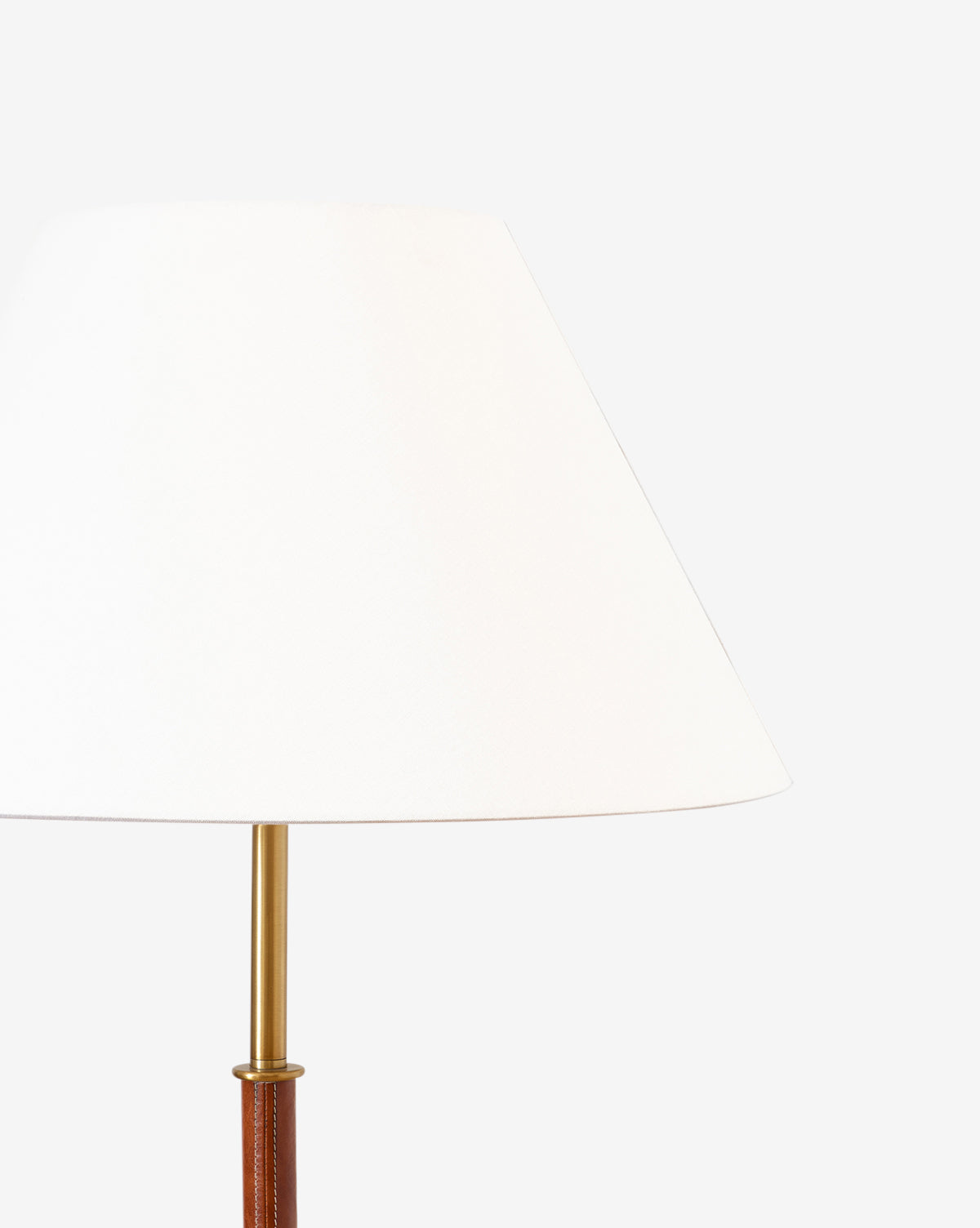 A close-up of the Elijah Floor Lamp with a white cone-shaped shade, brass pole neck, and brown base with leather accent, shown against a plain white background by McGee & Co.