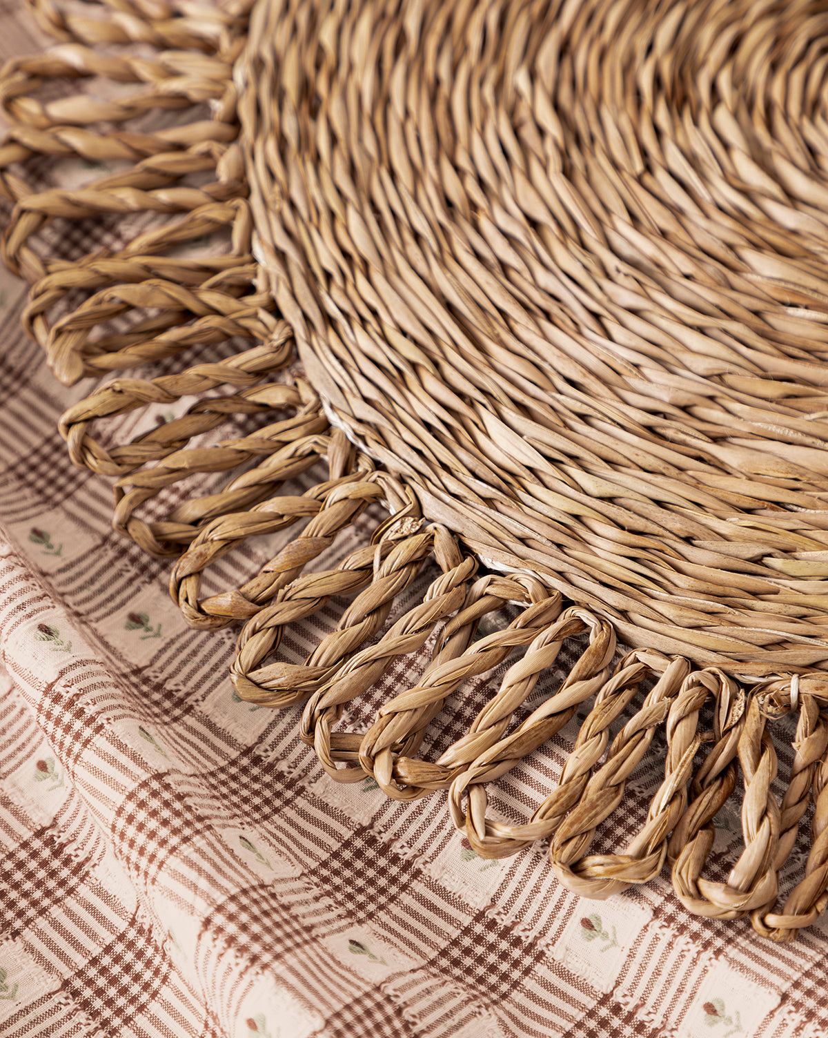 Close-up of the McGee & Co. x Loeffler Randall Elise Seagrass Placemat with looped edges, styled on a beige and brown plaid tablecloth featuring small floral details for charming tabletop decor, by McGee & Co.