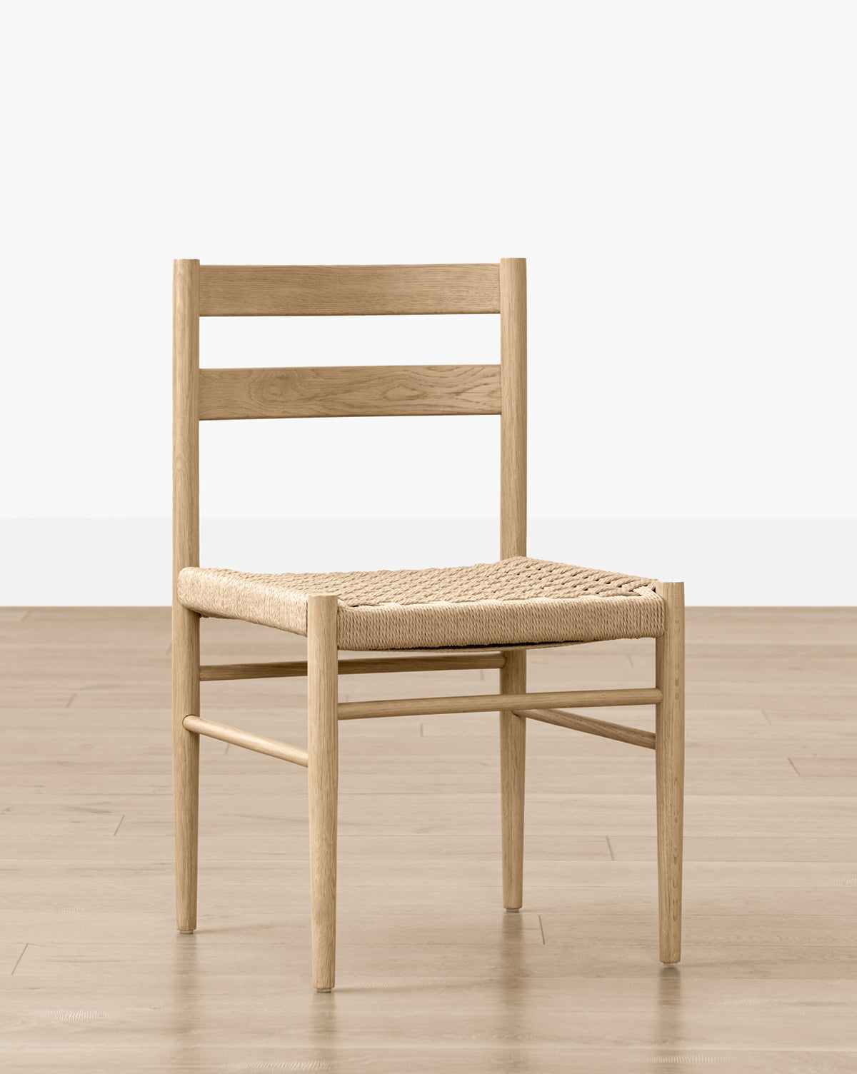 The Eloise Woven Chair is a minimalist wooden dining chair with a simple ladder-style backrest, ideal for dining rooms, by McGee & Co. Shown on a light wood floor against a plain white background.