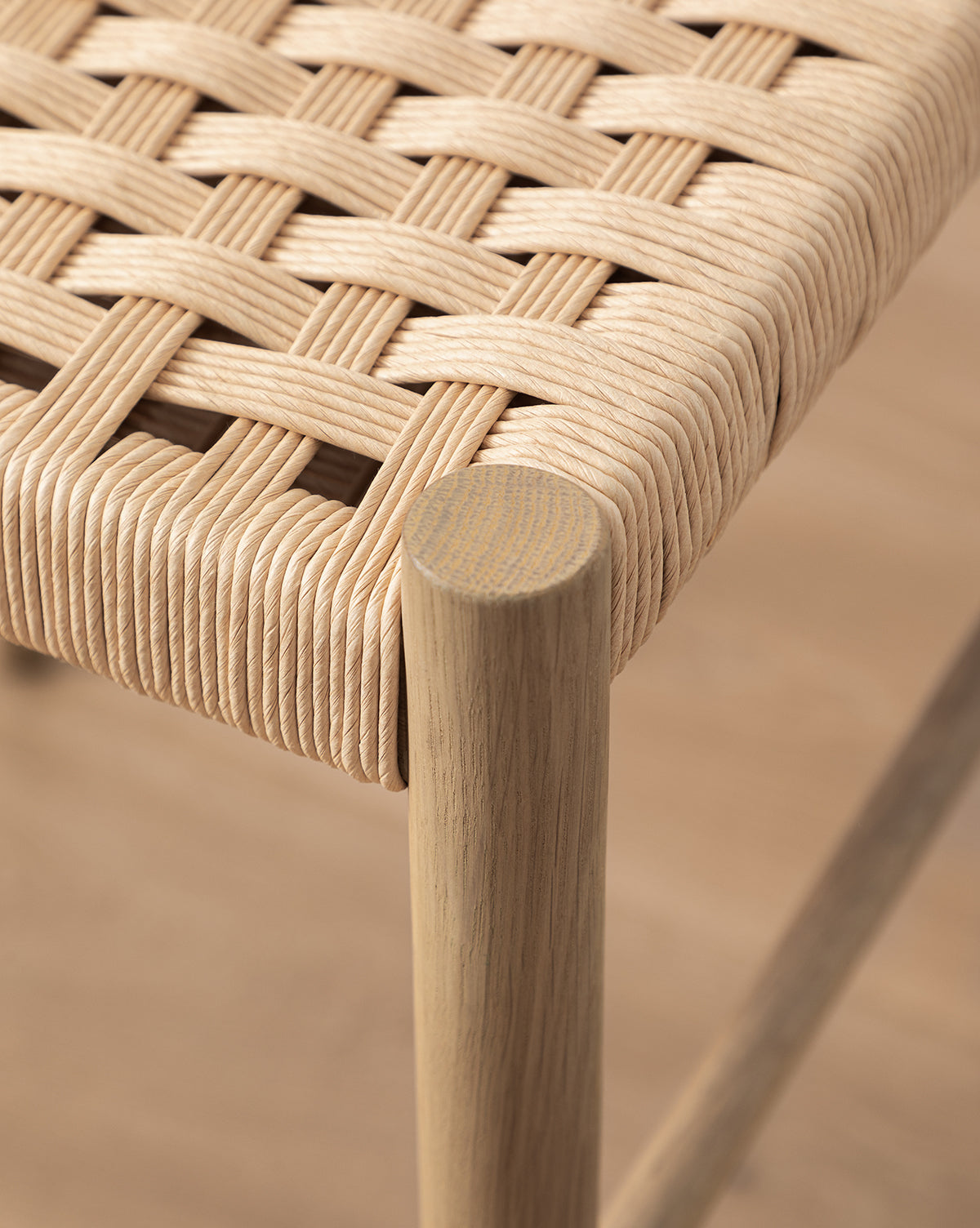 Close-up of the Eloise Woven Counter Stool, featuring a light wood frame and tightly interlaced natural fiber seat that highlights its authentic Danish design, set against a wooden floor background by McGee & Co.