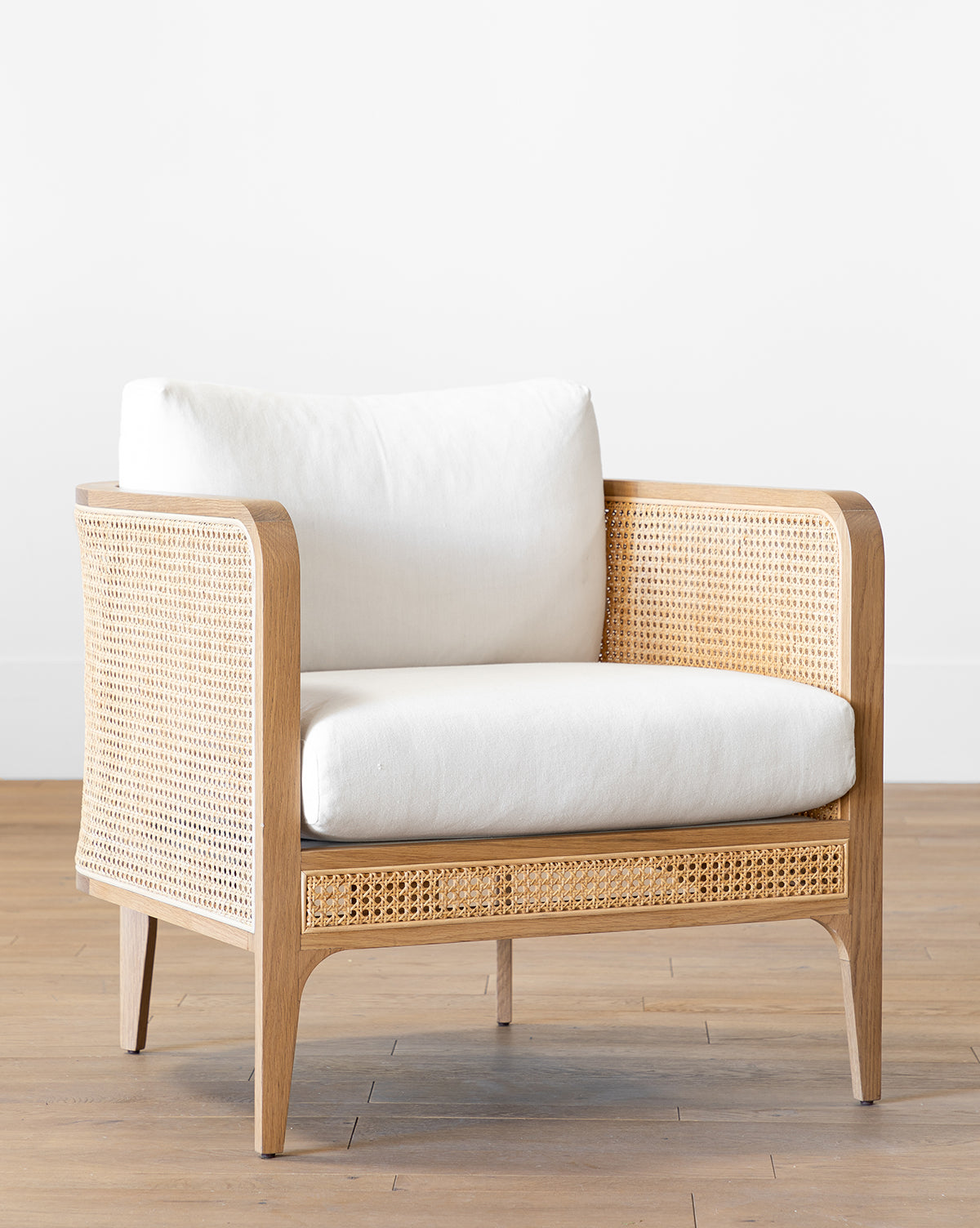 The Elowyn Lounge Chair features a solid oak frame, natural caning on the sides and base, and plush white cushions, making it a modern statement piece for any room, by McGee & Co.