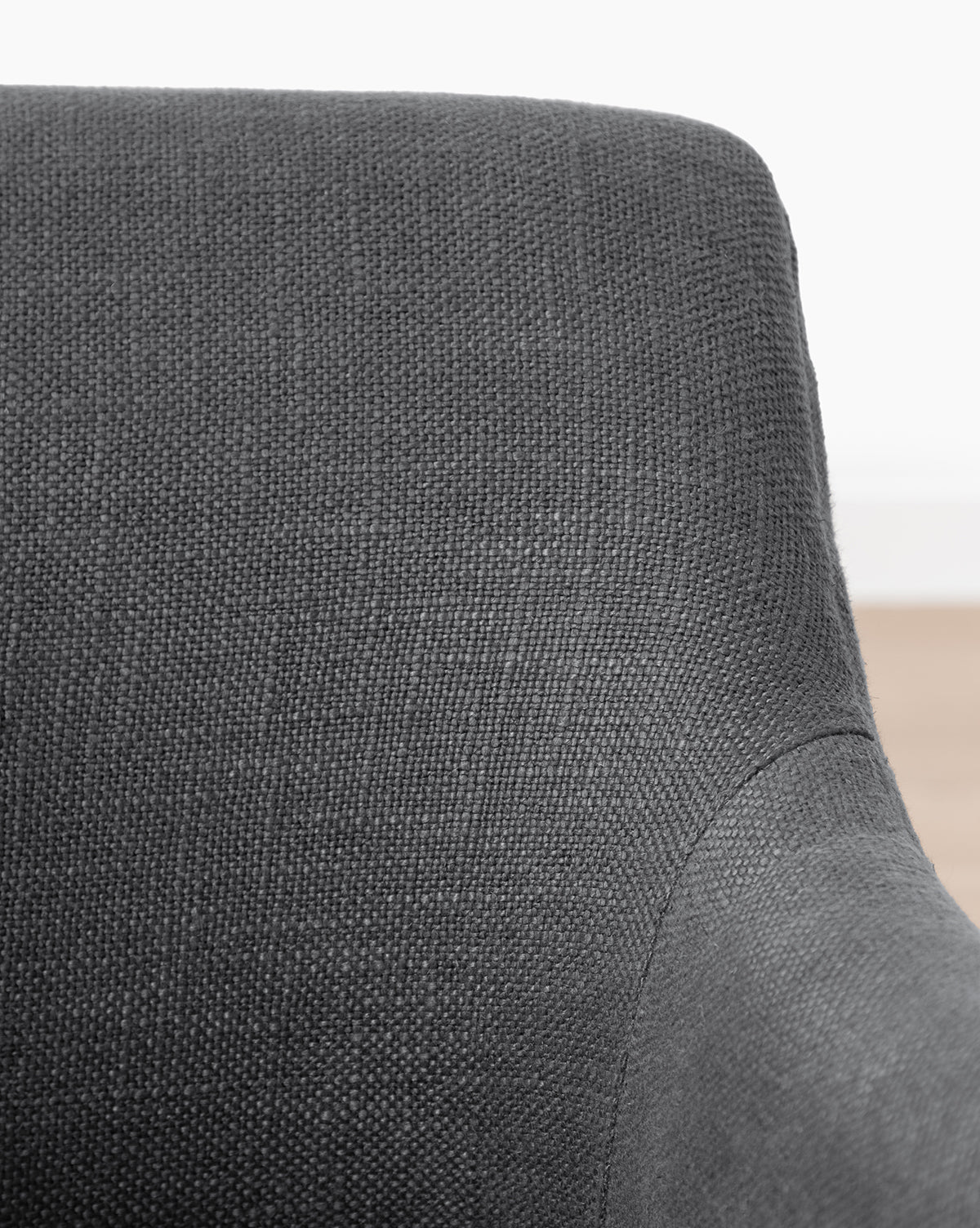 Close-up of the Elton Dining Chair, showcasing its dark gray linen-blend upholstery, smooth curved backrest, and visible seat and armrest—ideal for modern dining areas with a light backdrop, by McGee & Co.