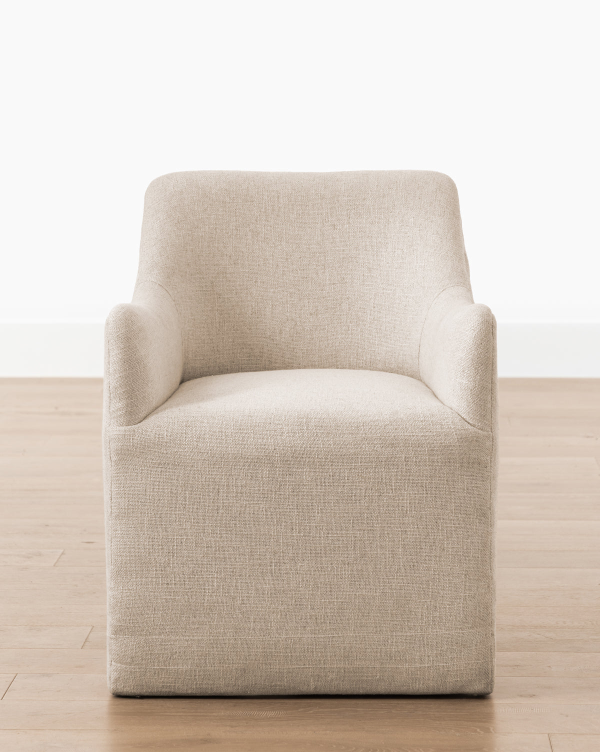 The Elton Dining Chair, upholstered in modern beige linen blend with a boxy shape and curved arms, sits on a light wooden floor—perfect for elevating dining spaces against a plain white background, by McGee & Co.