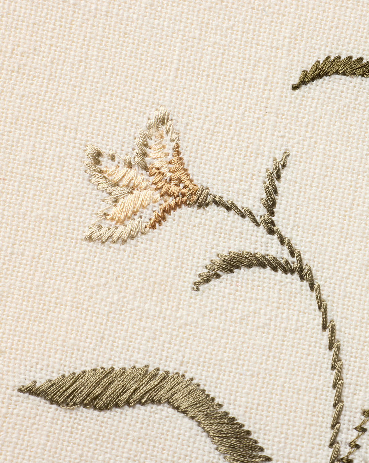Close-up of Embroidered Pixie Flowers on beige fabric, showcasing a light orange and cream bloom with olive green leaves and stem. Intricate stitching makes it ideal as botanical wall art or unique cotton wall decor, by McGee & Co.