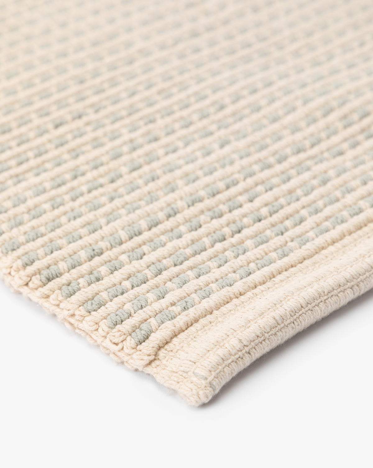 Close-up of the Emina Bath Mat in beige and light blue, crafted from 100% cotton. Features a raised, grid-like texture and neatly finished edge—perfect for updating your bathroom decor.