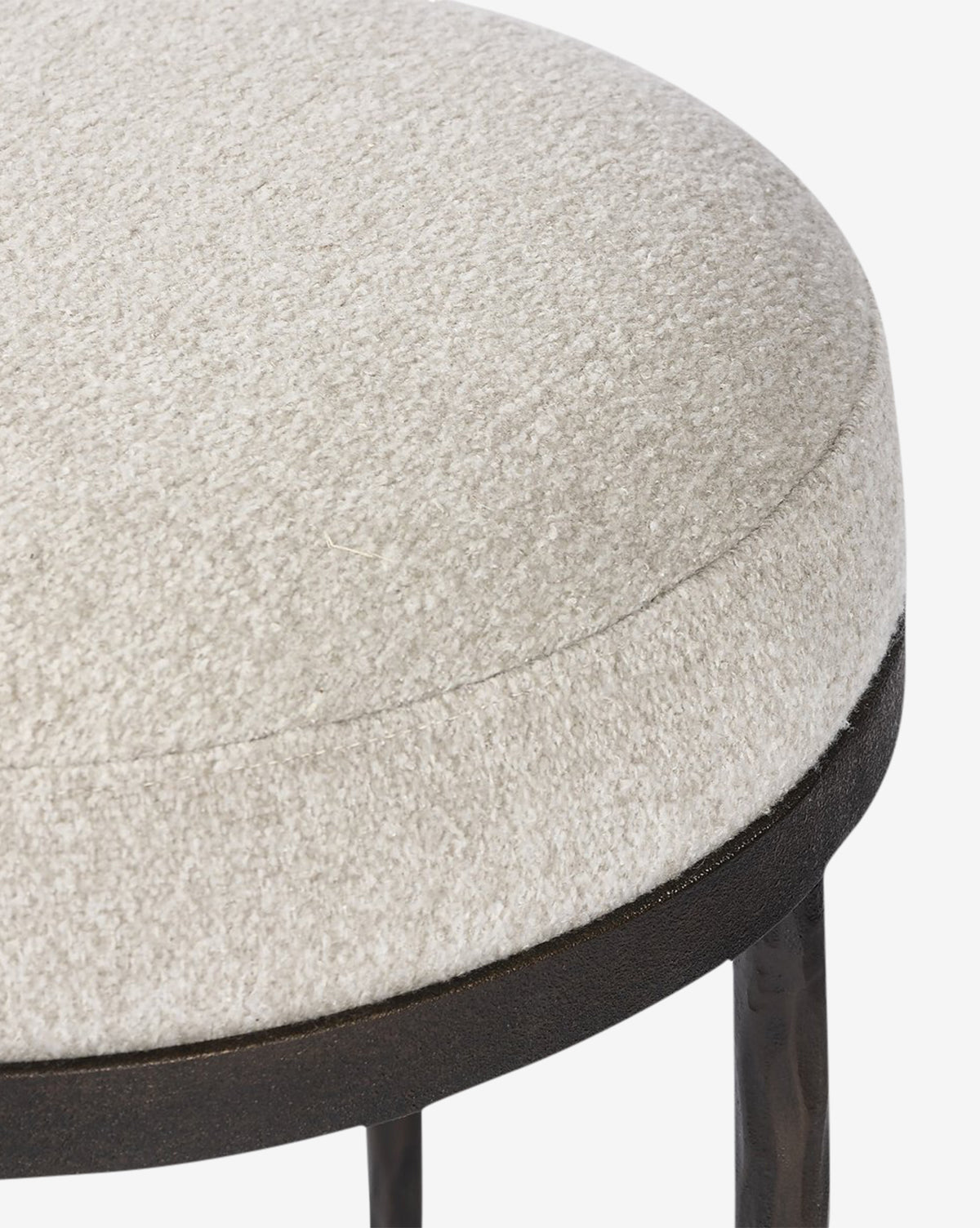 Close-up of the Emmett Stool by Four Hands—a round, upholstered cocktail ottoman featuring textured off-white fabric and a dark hammered bronze base with slim legs, making it a stylish accent for any room. McGee & Co.