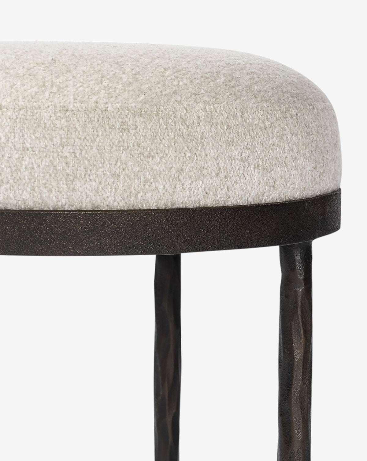 Certainly! Here’s your blended sentence: The Emmett Stool by Four Hands features a round hammered bronze base, textured light beige upholstered seat, dark metal rim, and two black hammered metal legs—an ideal accent piece against a white background by McGee & Co.