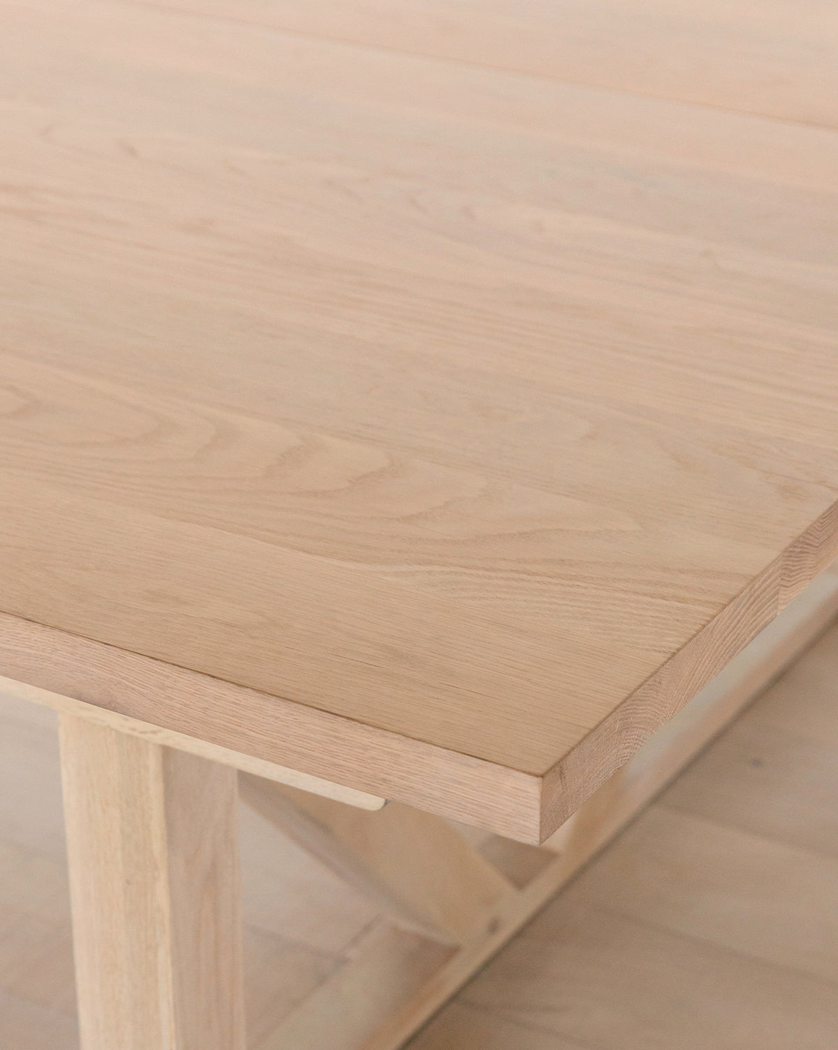 A close-up of the Emory Extension Dining Table shows its solid oak construction, smooth natural finish, and visible wood grain. The tables architectural base and part of the floor are also partially visible by McGee & Co.