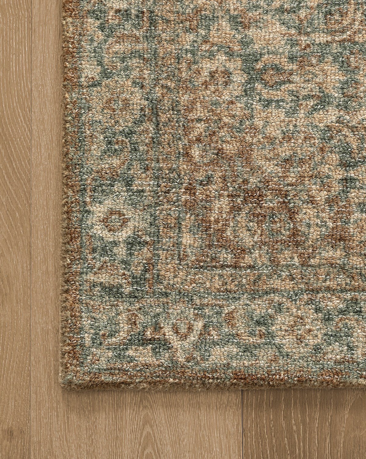 A close-up of the Endicott Hand-Tufted Wool Rug showcases its ornate, traditional design in beige, brown, and blue tones, lying on a light wooden floor, by McGee & Co.