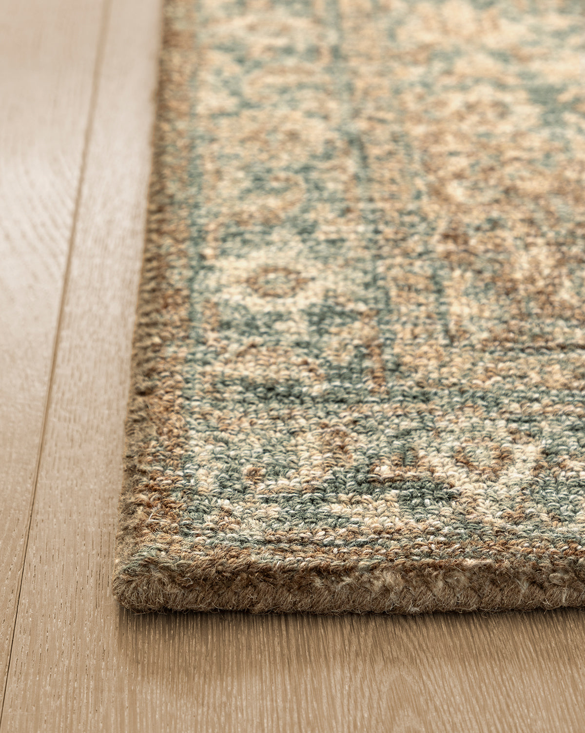 A close-up of the corner of the Endicott Hand-Tufted Wool Rug, featuring a blue and beige geometric pattern, placed on a light wood floor, by McGee & Co.