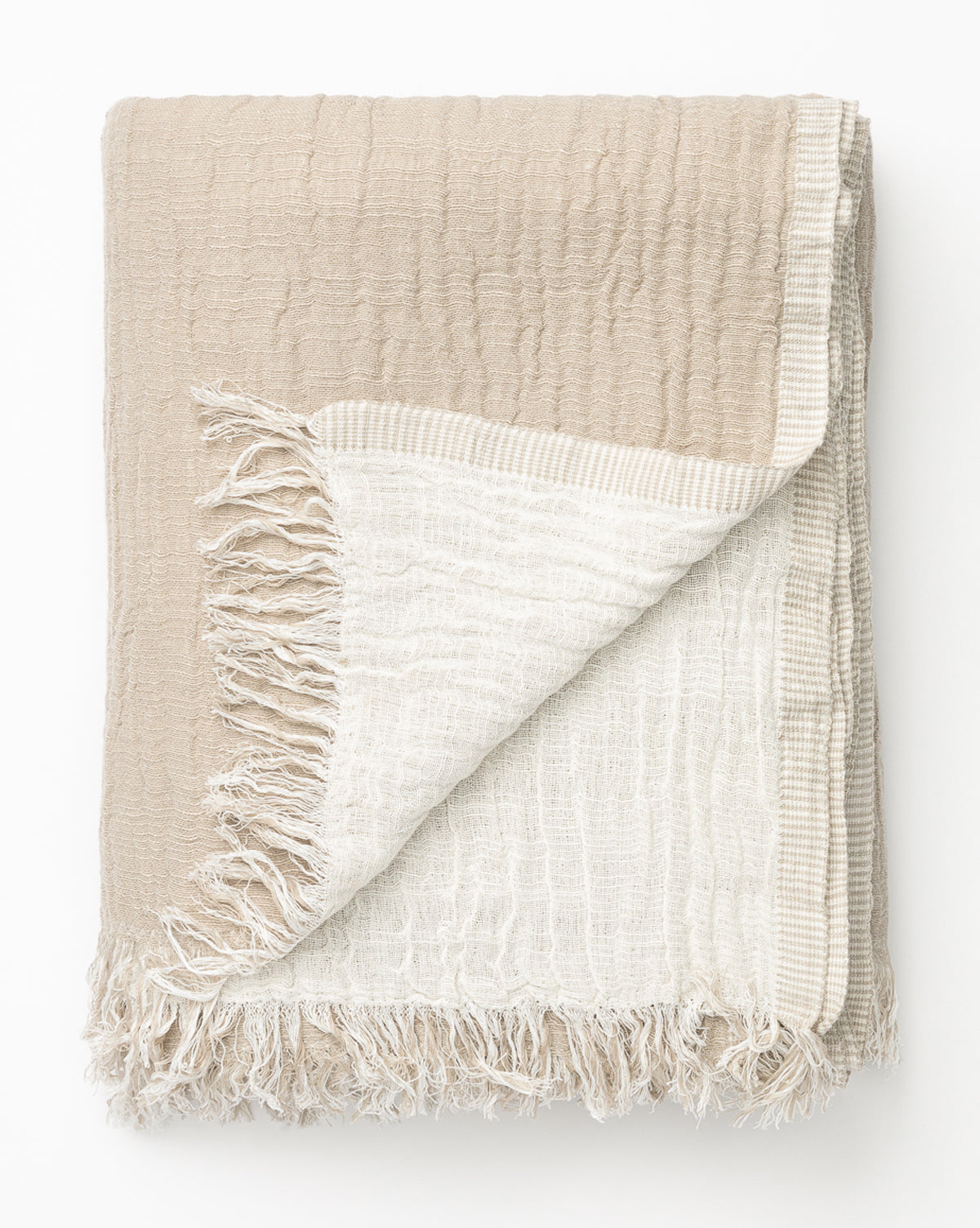 The Ermessa Oversized Throw is a cozy, oversized blanket made from a soft cotton-bamboo blend. It features beige on one side, off-white on the other, a textured finish, and frayed edges for added character.