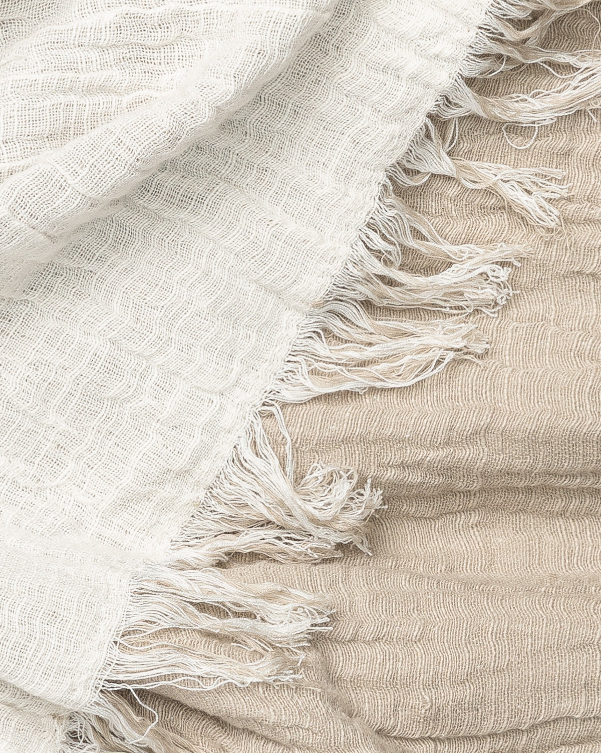 Close-up of two Ermessa Oversized Throw blankets—one off-white, one light beige—crafted from a soft cotton bamboo blend with fringed edges and a subtle crinkled texture.
