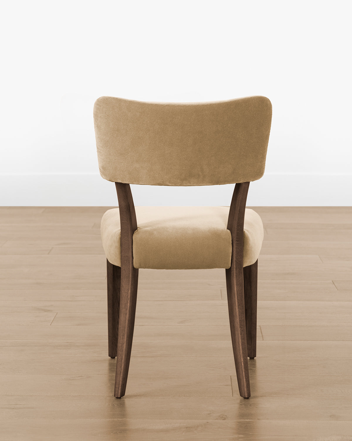 The Etienne Dining Chair (Ready to Ship) has a beige upholstered seat and backrest, curved wooden legs, and frame, offering a modern vintage style—perfect for light wood floors and plain white walls, by McGee & Co.