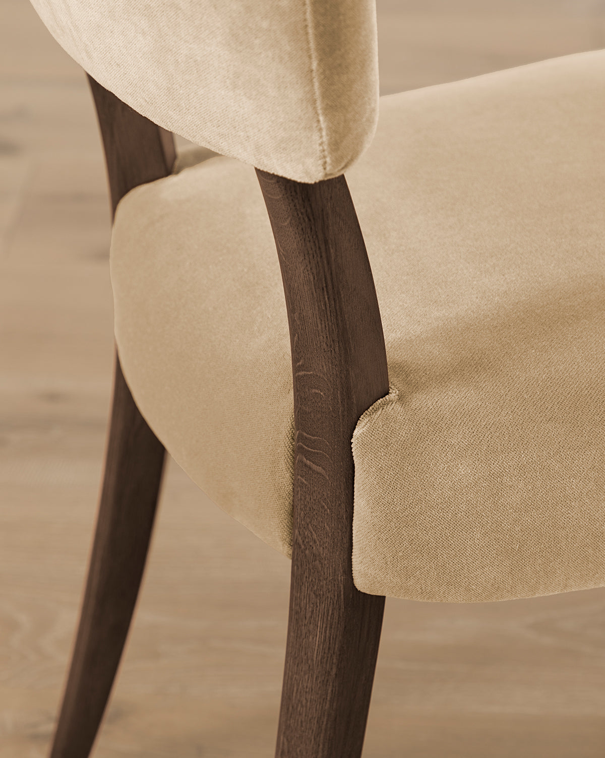 Close-up of the Etienne Dining Chair (Ready to Ship) with customizable light beige upholstery and curved dark wood legs, shown on a light wood floor by McGee & Co.