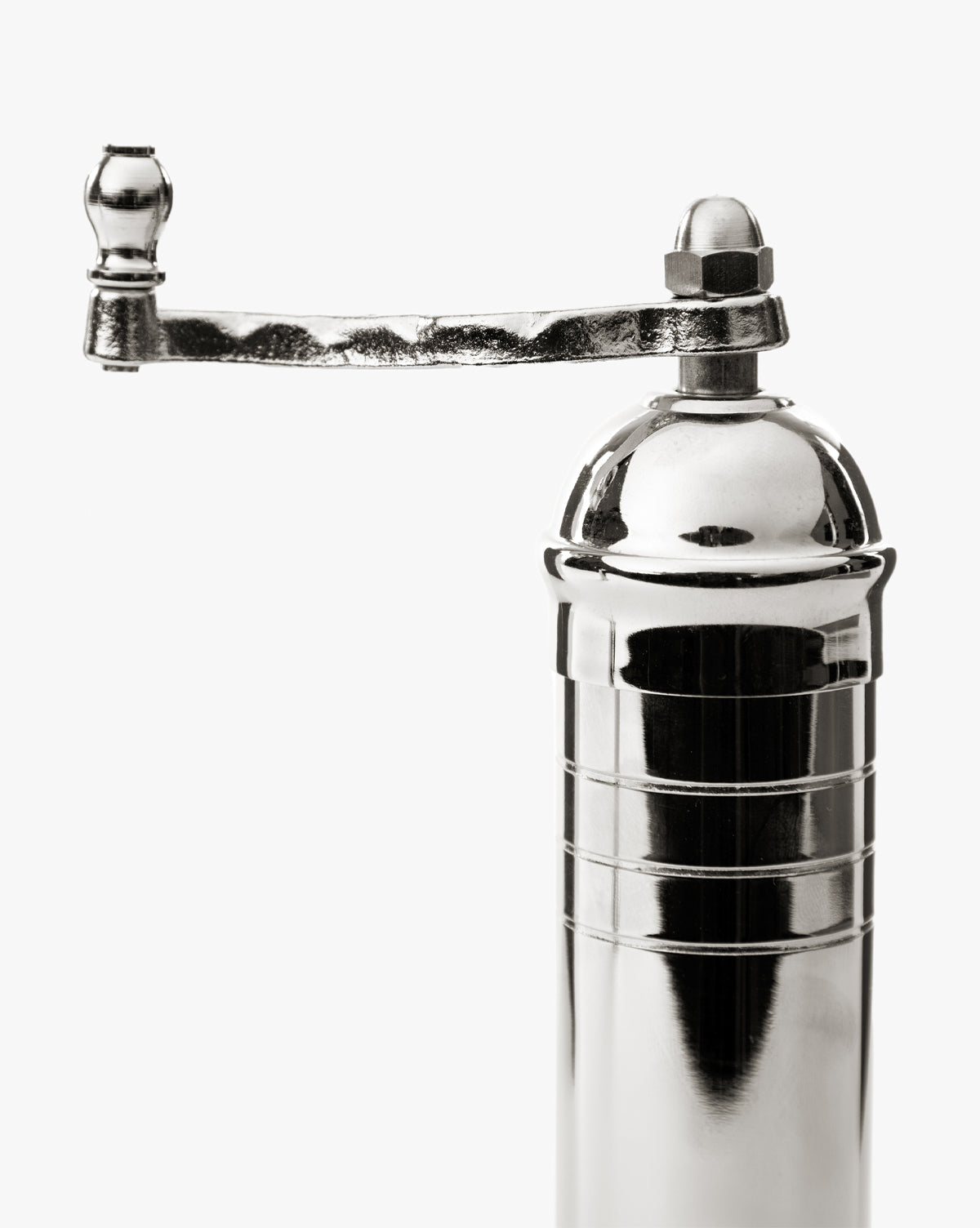 A close-up of the European Chrome Pepper Mill, featuring a shiny chrome finish, a curved hand crank handle, and an adjustable steel grinding mechanism, set against a plain white background, by McGee & Co.