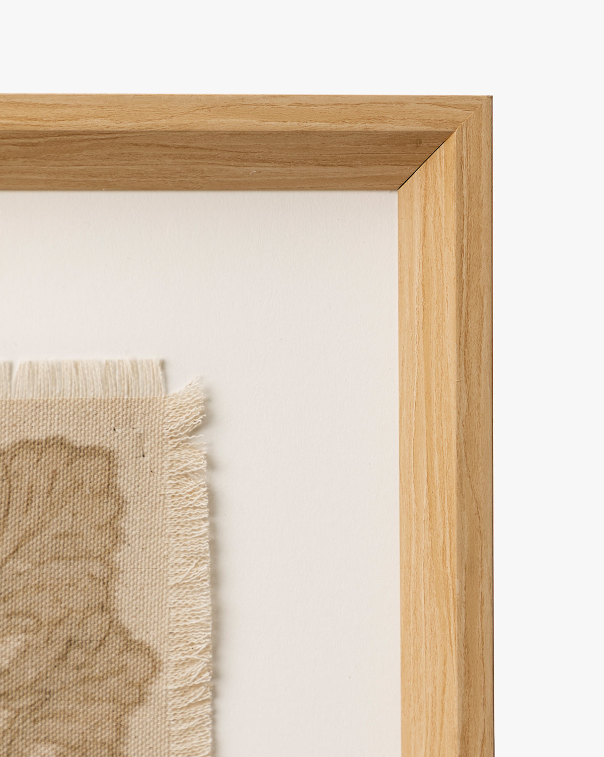 A close-up of the European Flare frame’s natural woodgrain corner surrounds vintage-style wall art—beige fabric with frayed edges and a subtle leaf design—displayed on a white background, by McGee & Co.
