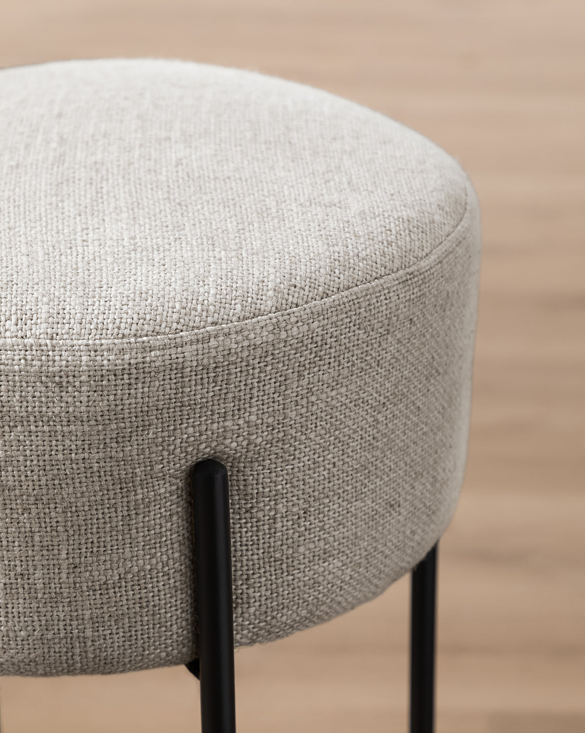 Close-up of the Makerspalm Evander Counter Stool, featuring industrial design with light gray textured fabric and black metal legs, set against a blurred wooden floor—ideal for stylish modern kitchen seating. McGee & Co.