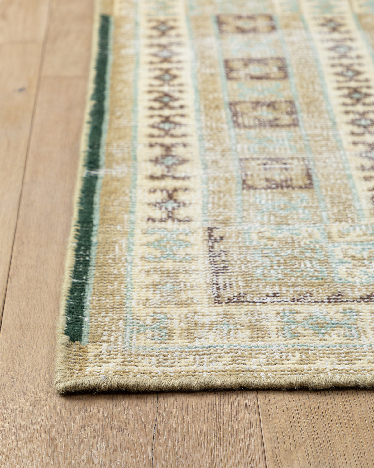 A close-up of the Evangeline Hand-Knotted Wool Rug’s corner on a light wooden floor, showcasing its durable wool texture and geometric border design, by McGee & Co.