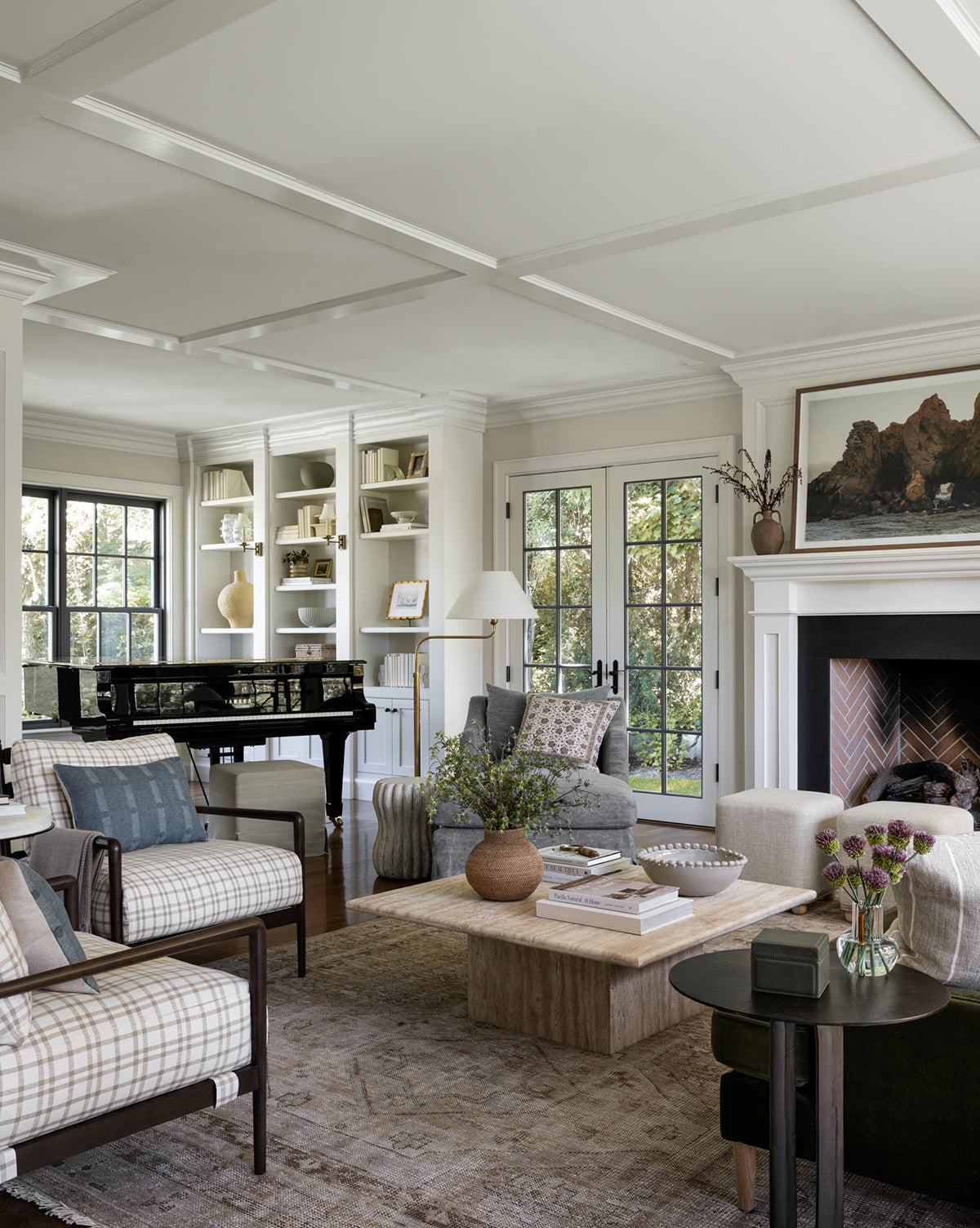 A bright, elegant living room with large windows, a black grand piano, built-in white shelves, a cozy armchair, fireplace with art above, and neutral furniture arranged on the Charlot Hand-Knotted Rug, by McGee & Co.