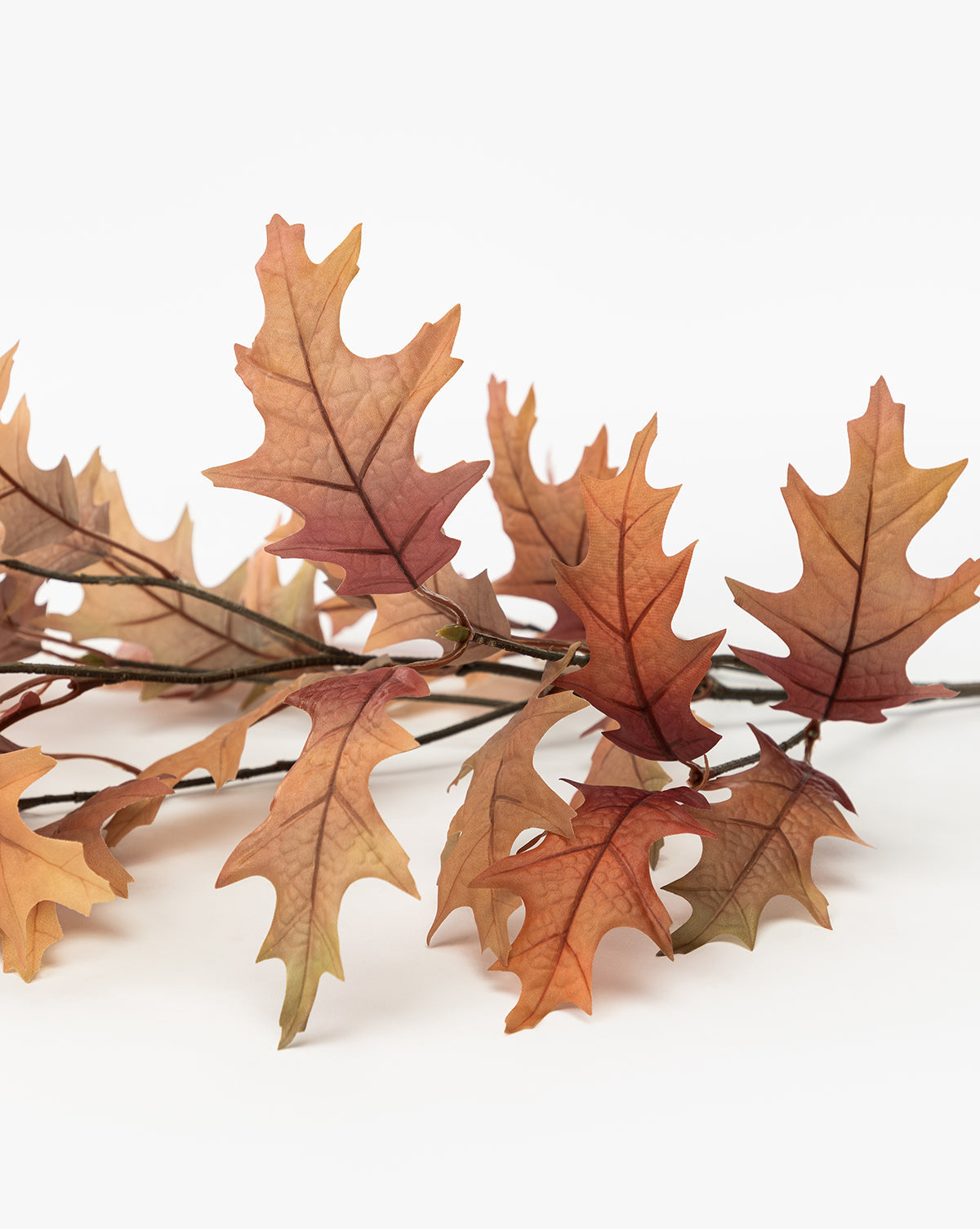The Faux Autumn Oak Stem features branches with oak leaves in brown, orange, and red shades arranged against a white background, making it ideal for autumn décor.