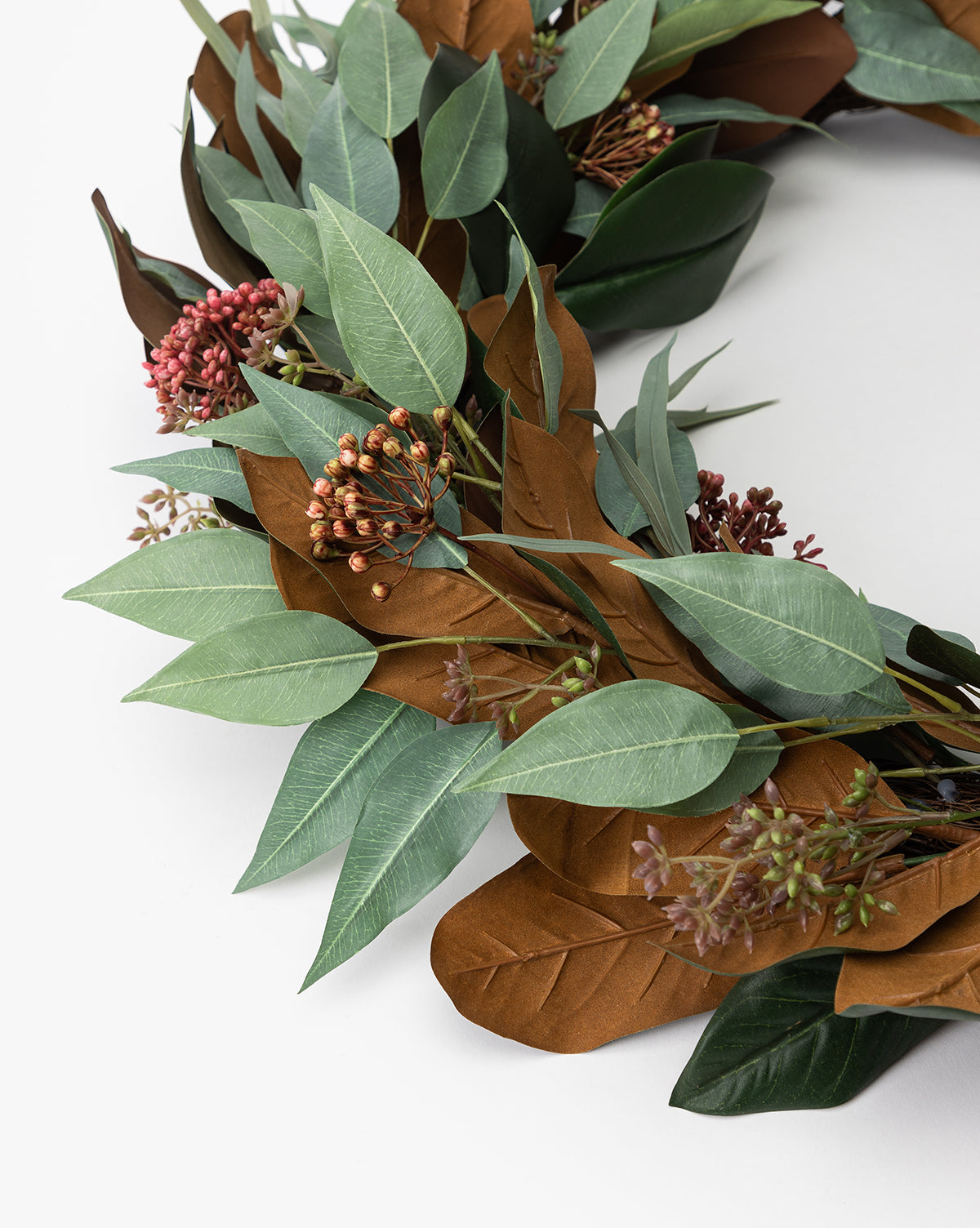 A close-up of the 30 Faux Magnolia & Eucalyptus Wreath, featuring green and brown leaves with red and purple berry clusters, arranged on a white background.