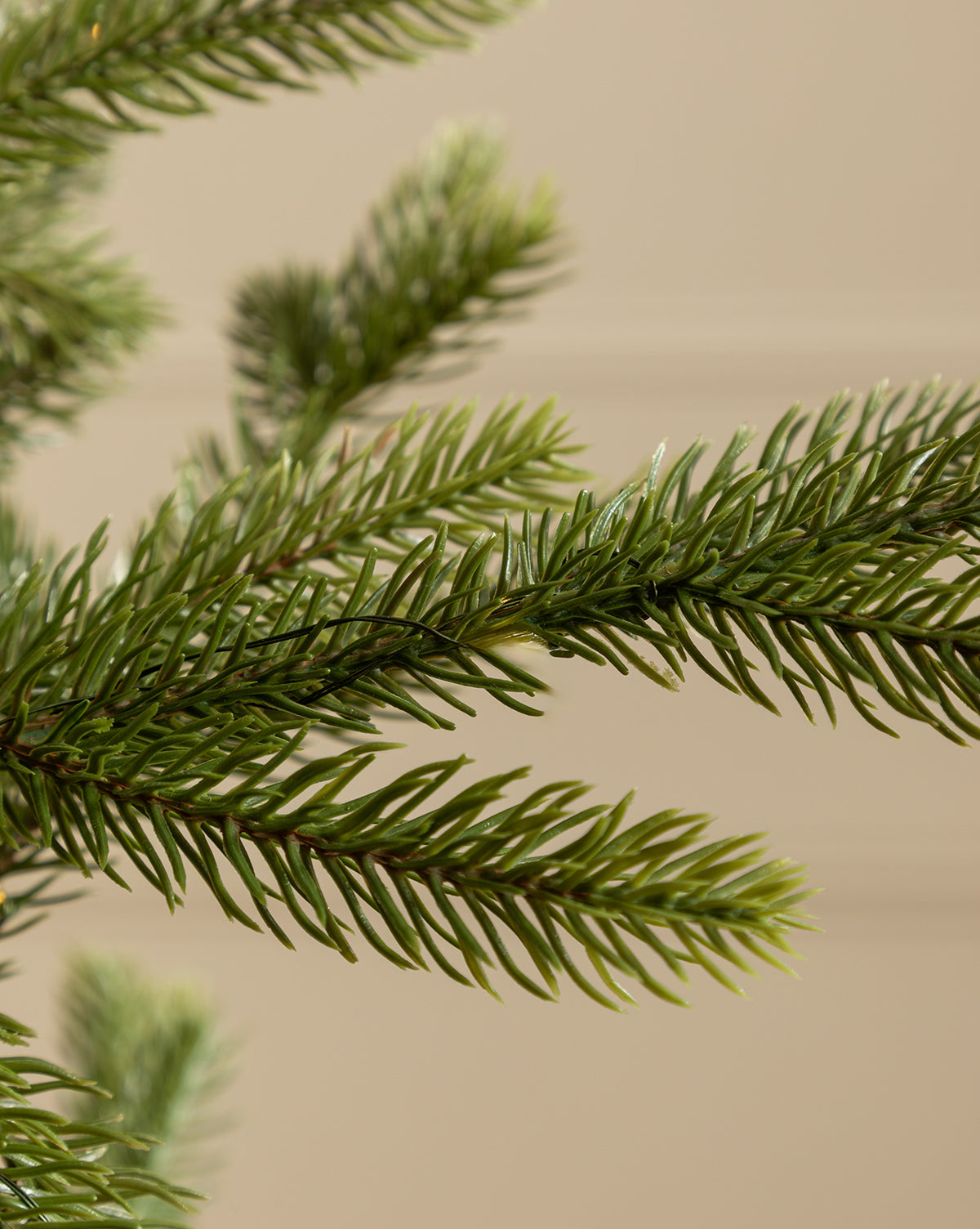 Close-up of dense green needles on the Faux Spruce Pre-Lit Potted Tree, with realistic artificial evergreen branches set against a neutral beige background, by McGee & Co.