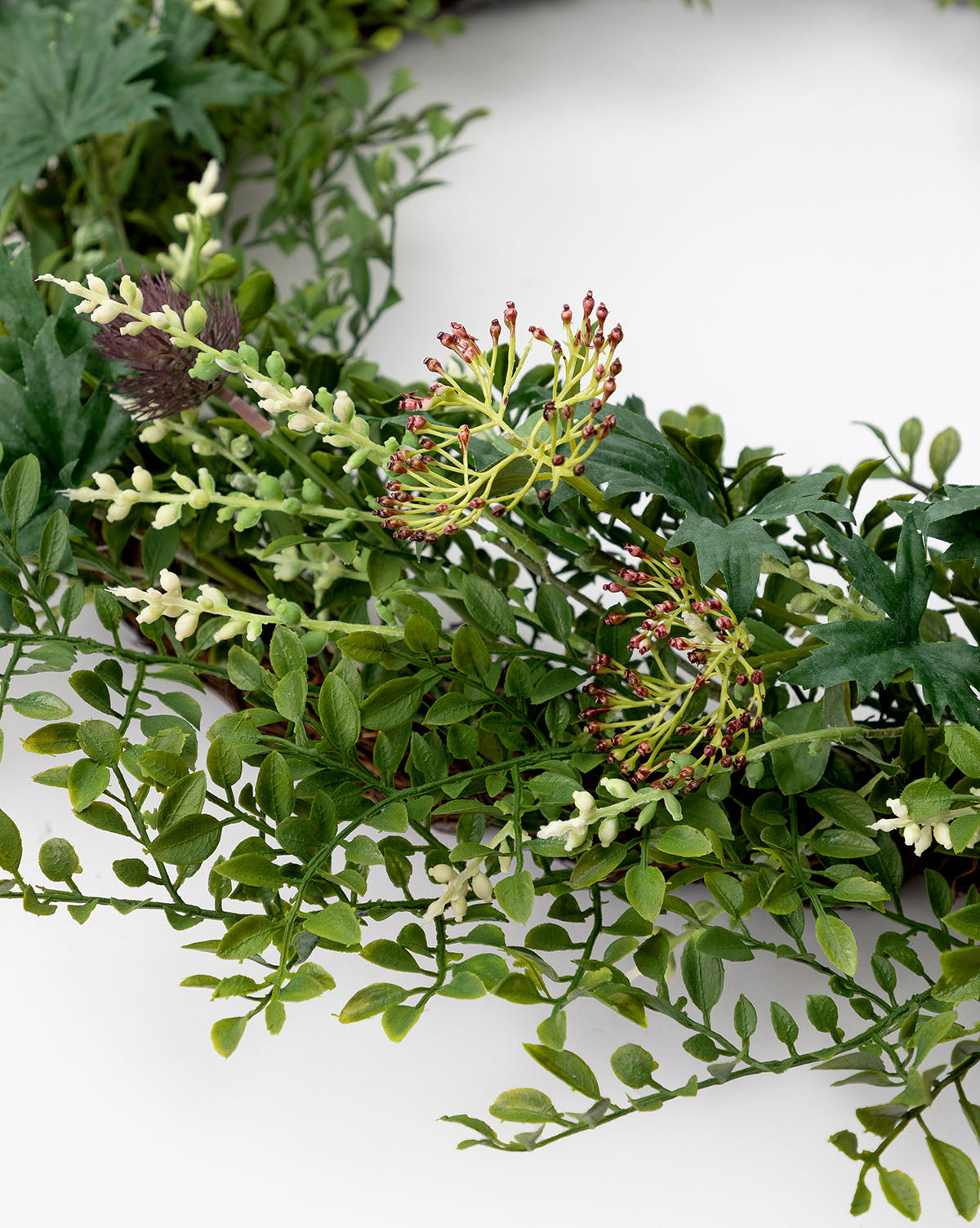 The Faux Summerset Wreath showcases lifelike greenery, small white buds, and spiky purple-tipped flowers—ideal for seasonal décor and beautifully displayed against a white background.