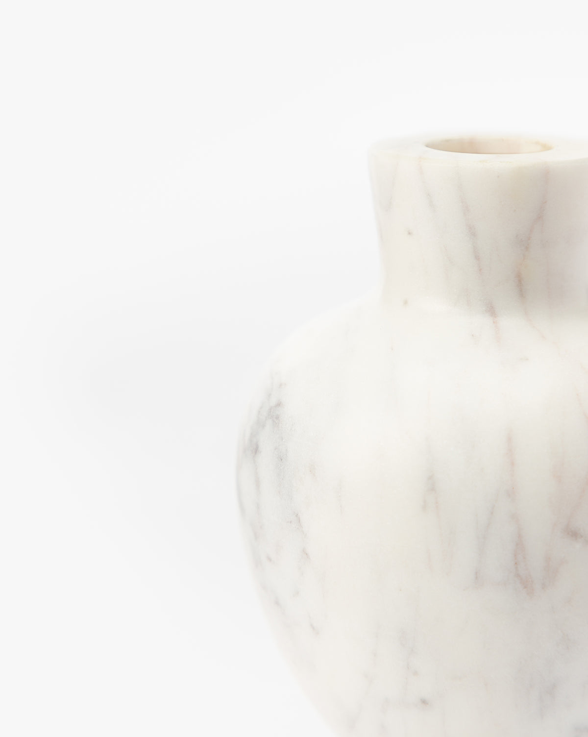 A close-up of the Fera Bud Vase, featuring white marble with subtle grey veining. This elegant vase’s rounded body and narrow neck are partially visible against a plain white background, by McGee & Co.
