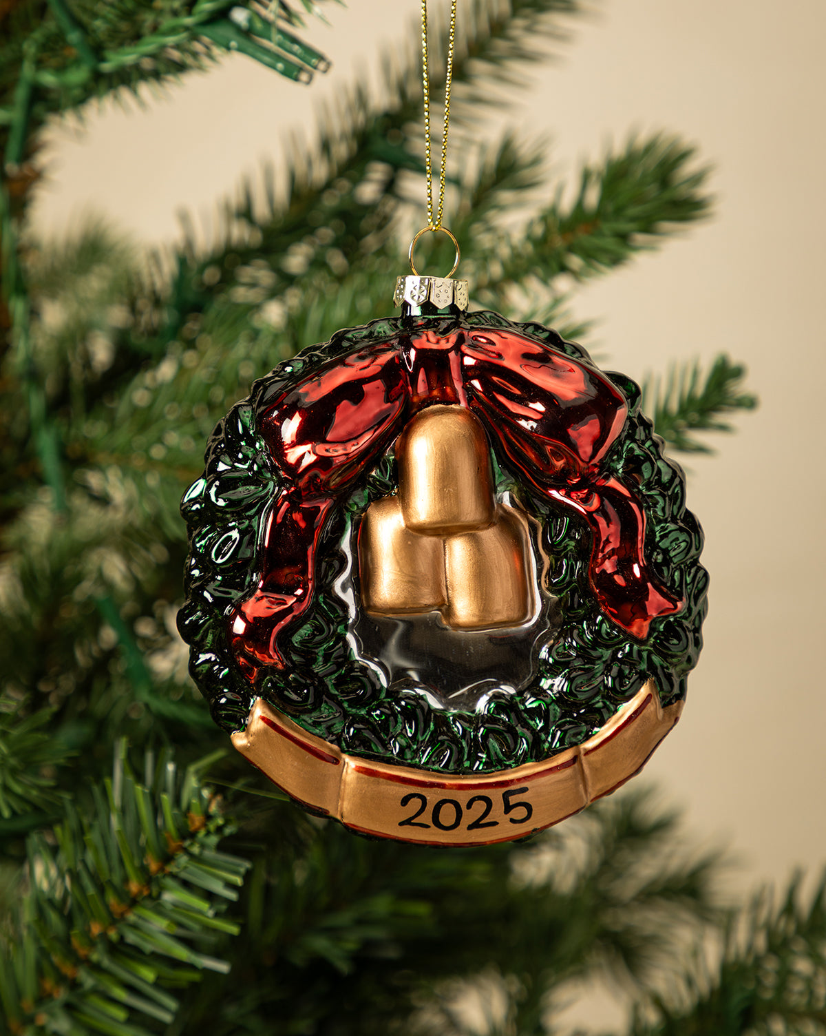 The Festive Wreath Ornament features a green wreath with a shiny red bow, three golden accents, and a gold "2025" banner—making it the perfect keepsake holiday ornament for your tree, by McGee & Co.