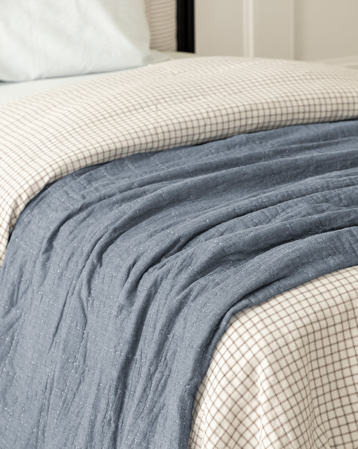 A neatly made bed features the Fitzgerald Kids Quilt—a textured blue-gray cotton quilt draped across cream and brown checkered sheets. A white pillow at the head creates a cozy look, perfect for twin kids’ bedding.