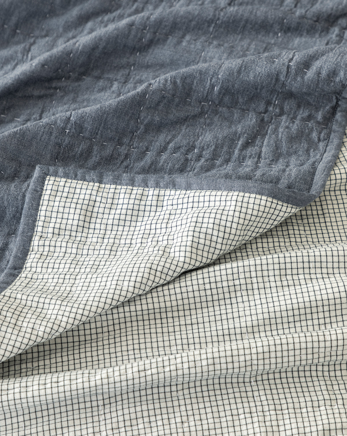 A close-up of the Fitzgerald Kids Quilt shows its dark blue quilted cotton top layer and white underside with a small black grid pattern. Slightly folded to display both sides, this blanket is ideal for twin kids’ bedding.