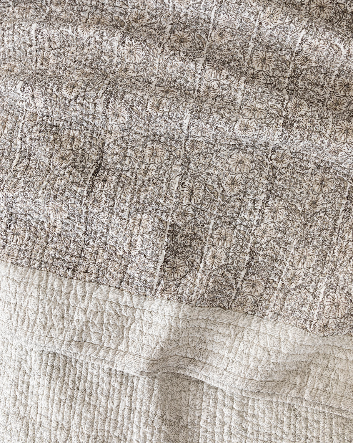 A close-up of the Floral Block Print Quilt displays its hand-quilted floral top, plain light bottom, intricate stitching, and soft fabric folds.