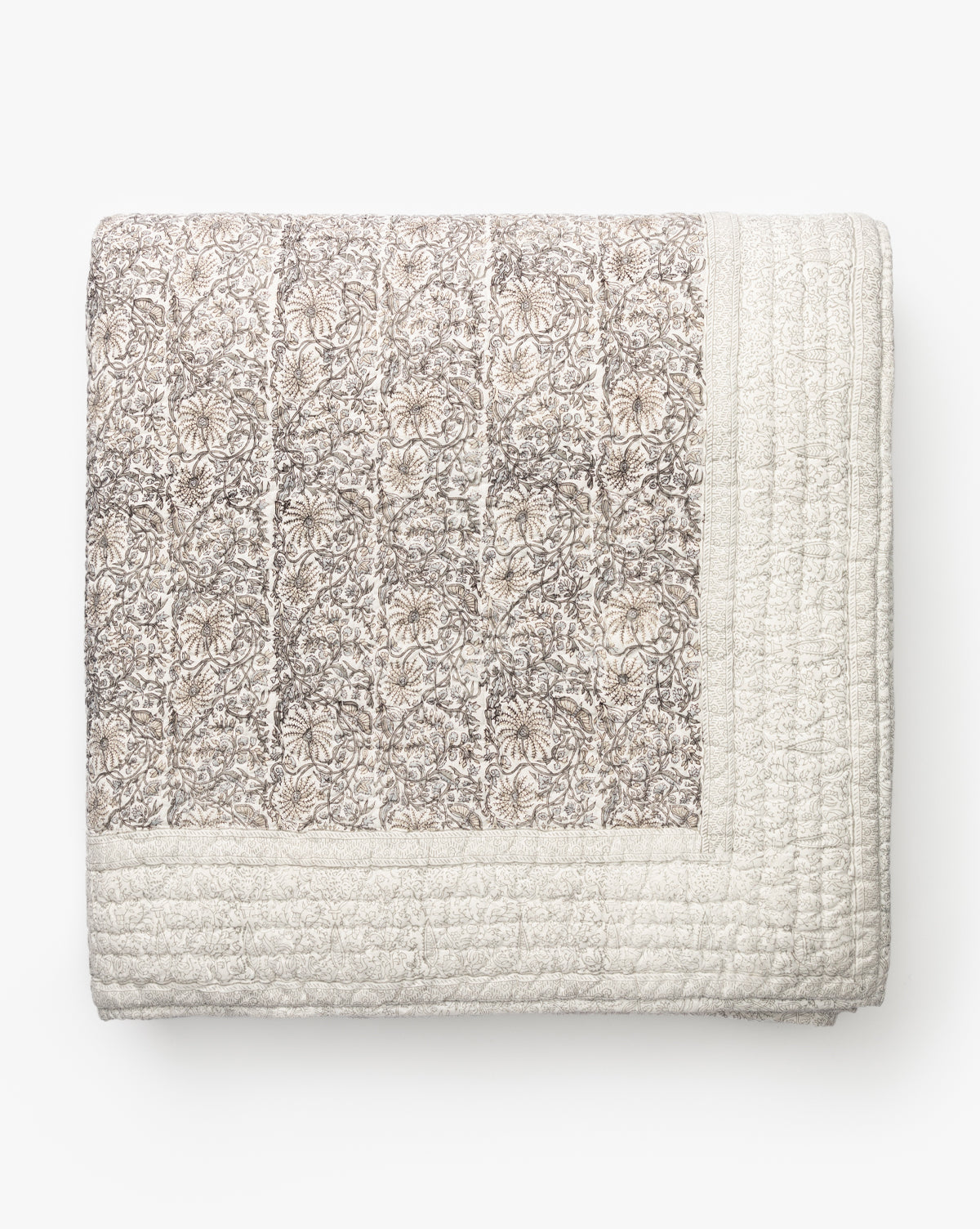 The Floral Block Print Quilt features a folded botanical design with muted floral patterns on one side and a solid, textured cream border on the other, shown against a plain white background.