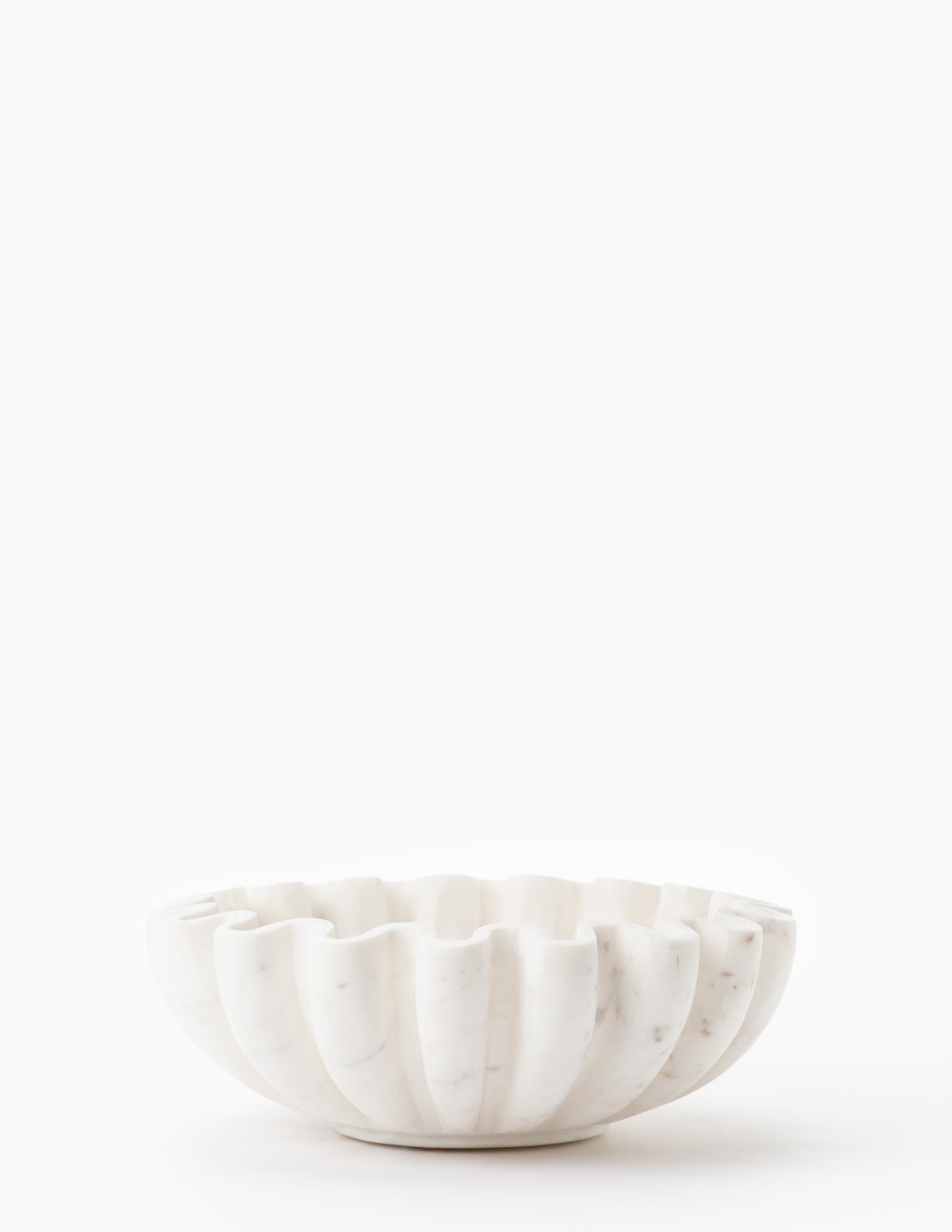 The Fluted Marble Bowl, featuring a scalloped design and elegant carved details, is displayed on a plain white surface against a white background.