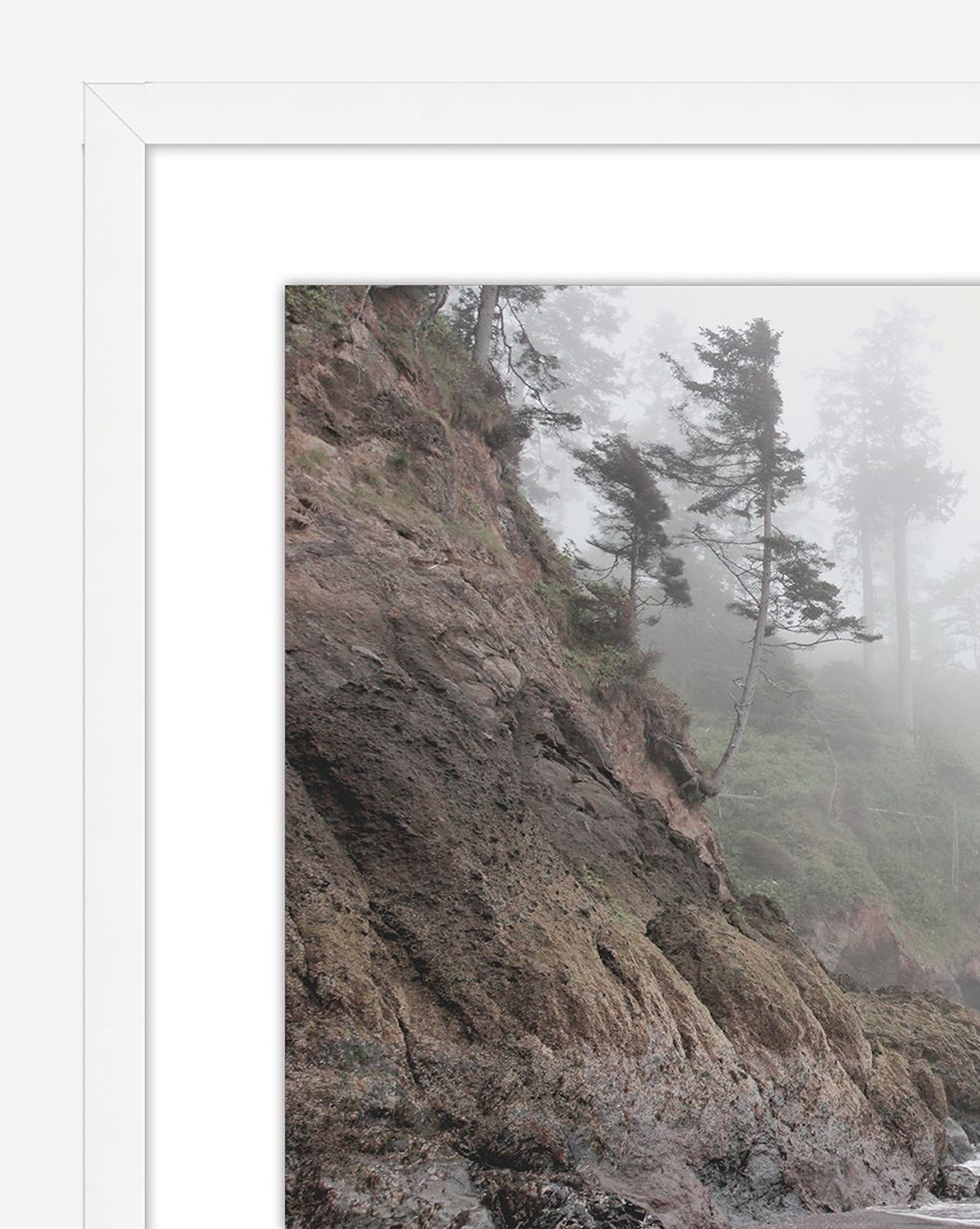 Foggy Shores is a framed photograph capturing a misty coastal cliff with rugged rocks and windswept trees, elegantly presented with a white mat and frame.