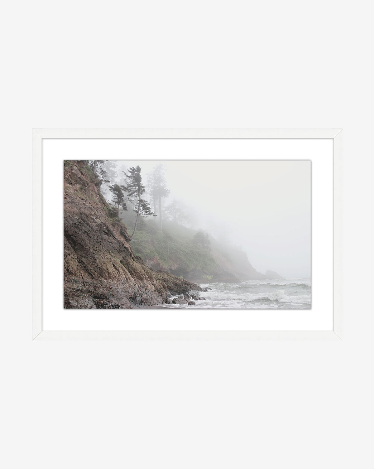 Foggy Shores—a framed photo capturing waves crashing onto rocky cliffs under fog and windswept trees—is stylishly displayed with a simple white mat and frame.