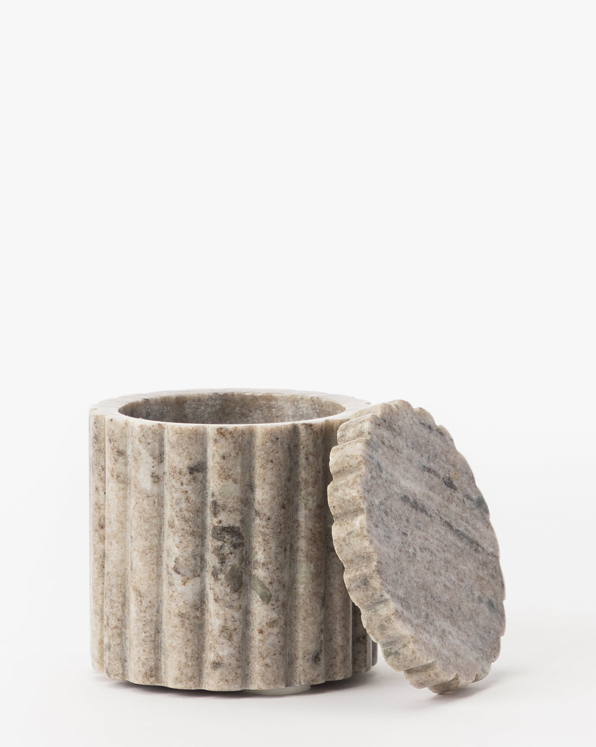 The Forster Marble Canister, crafted from organic marble with vertical grooves and a matching lid, leans against its open container. This small, round piece adds stylish home decor to any space against a plain white background.