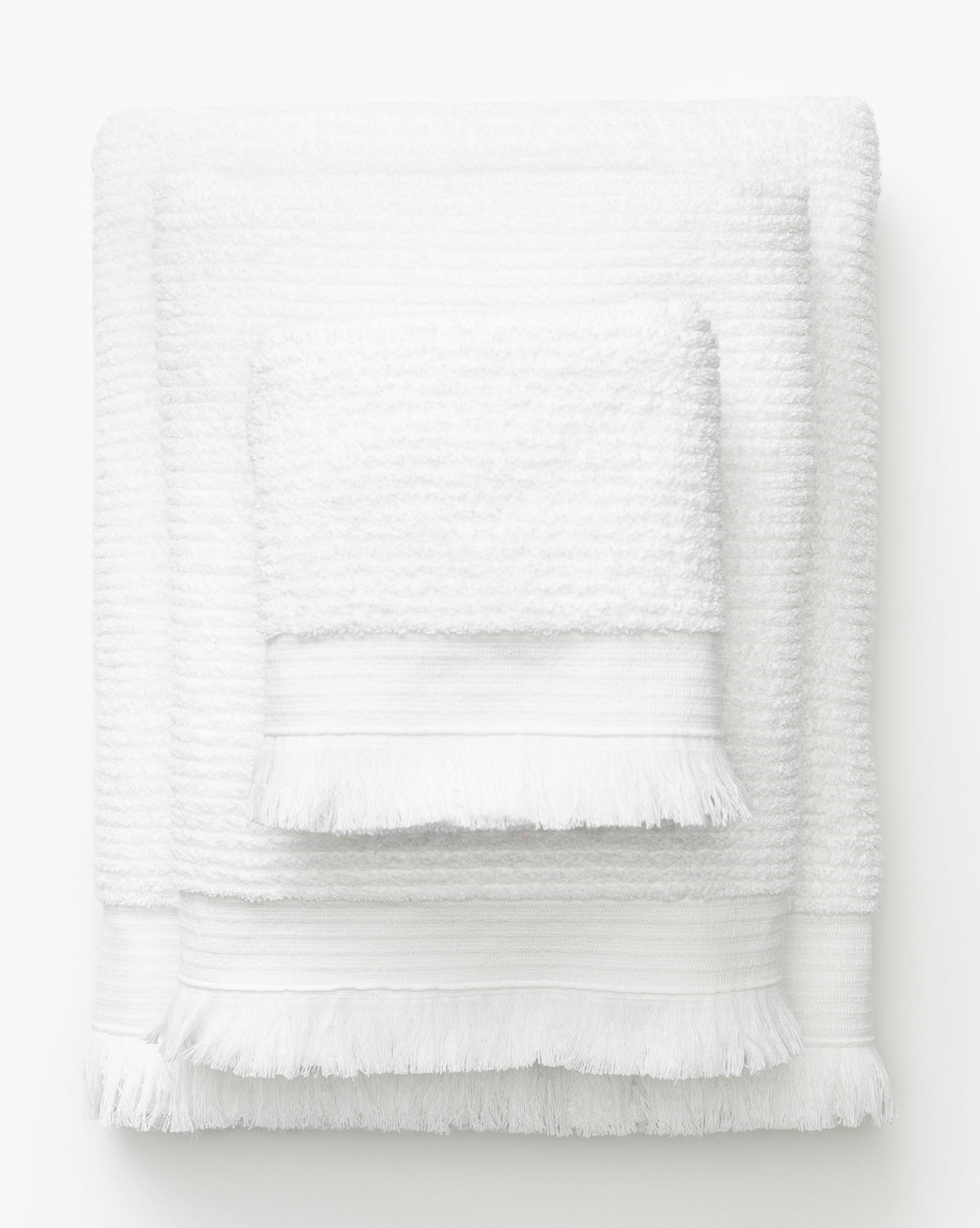 Three white towels of varying sizes from the Frayser White Bath Collection, each featuring fringed edges, are stacked together against a plain white background—an elegant addition to your bath essentials, by McGee & Co.