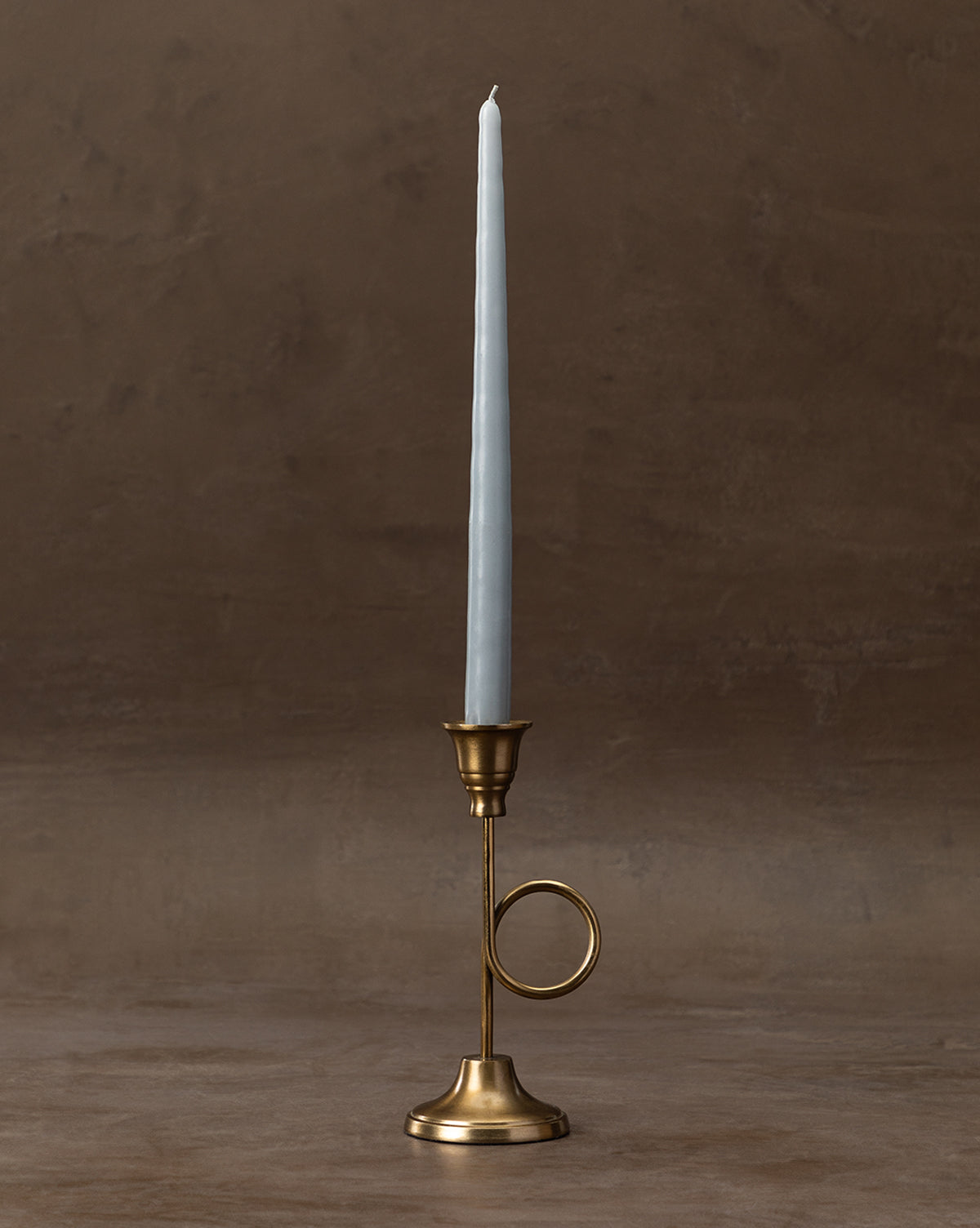 A tall, slender mauve taper candle sits in the French Horn Taper Holder with a circular handle, set against a neutral beige background—ideal for elegant holiday styling, by McGee & Co.