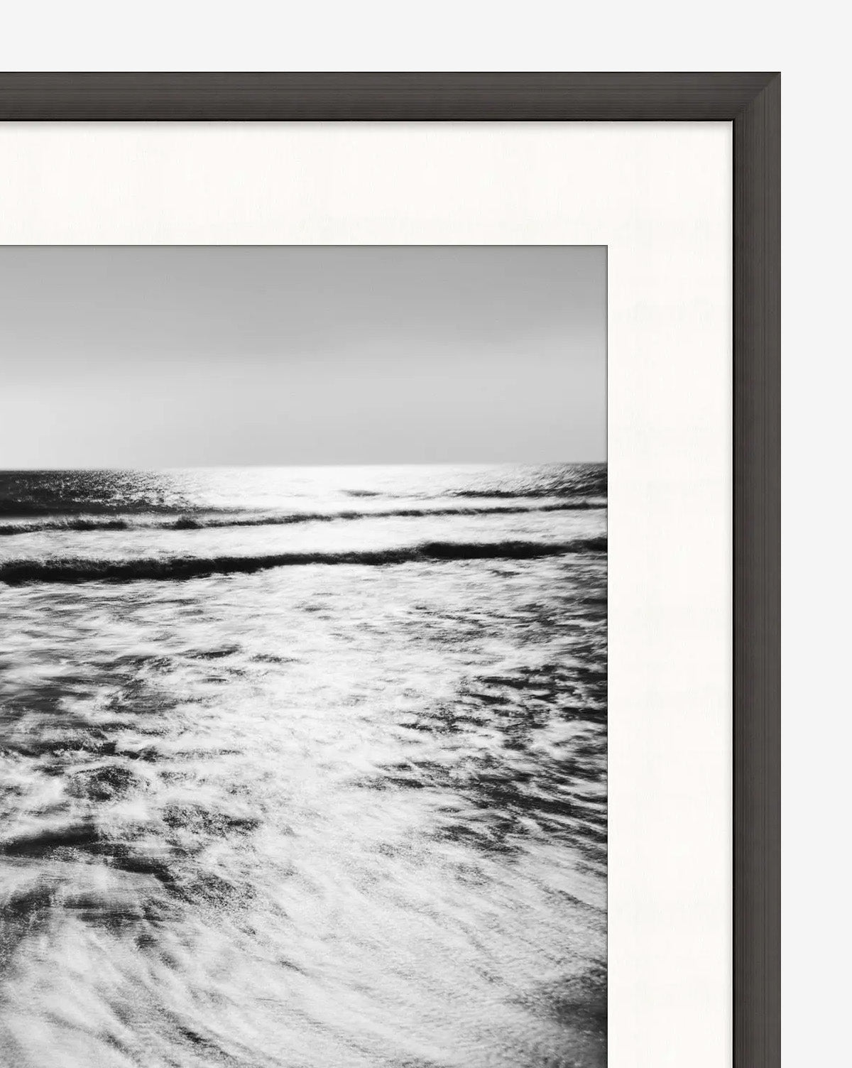 Frozen Waves captures ocean waves in black and white, sunlight glinting on the water. Presented as striking coastline wall art in a satin charcoal frame with a crisp white mat.