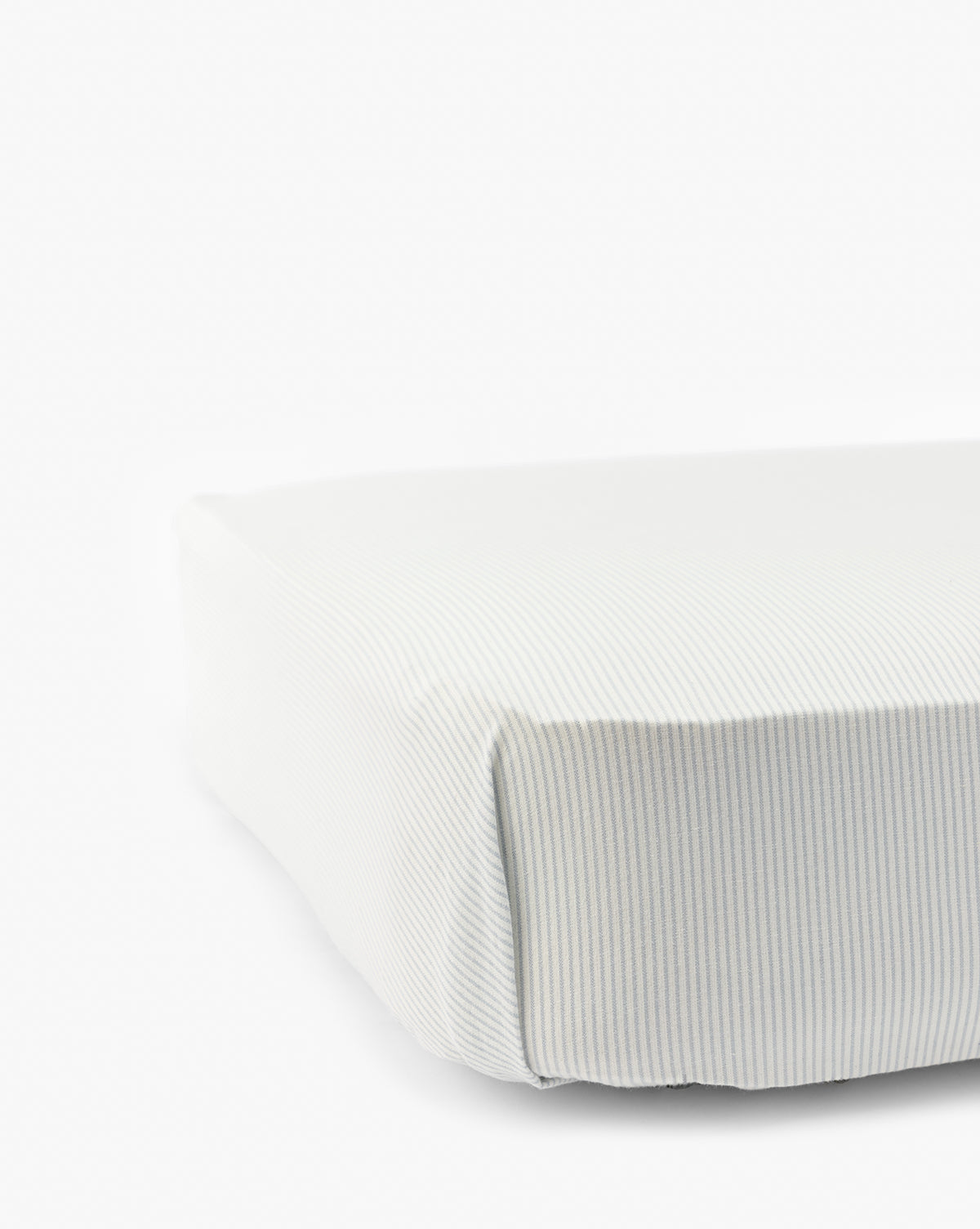 Close-up of a neatly made bed with the Fulton Stripe Crib Sheet, showcasing subtle light grey and white pinstripes on soft, smooth fabric. Ideal for childrens bedding, set against a plain white background by McGee & Co.