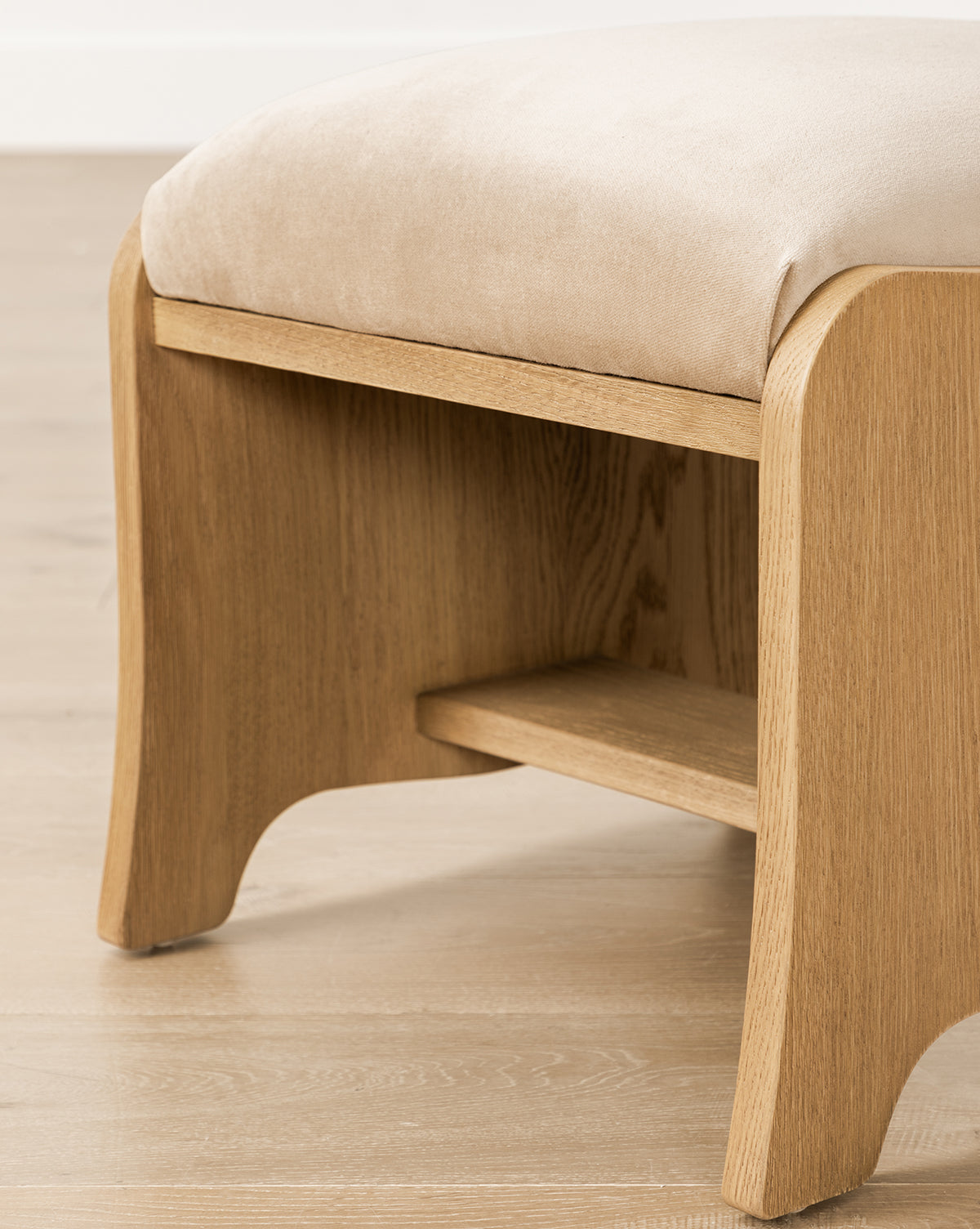 Certainly! Here’s your revised sentence with the exact string McGee & Co. blended at the end: A close-up of the Makerspalm Gable Ottoman featuring curved legs, a lower shelf, and a beige cushioned seat, shown on a light wooden floor by McGee & Co.