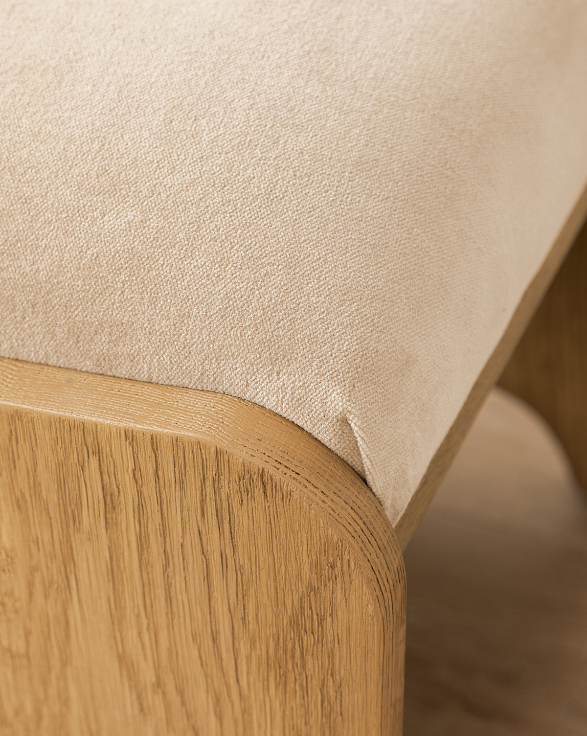 Certainly! Here’s your revised sentence with the exact string McGee & Co. seamlessly blended in at the end: Close-up of the Makerspalm Gable Ottoman featuring a smooth light beige Fawn Velvet seat and a sturdy, rounded wooden frame in a natural Drift Oak finish by McGee & Co.