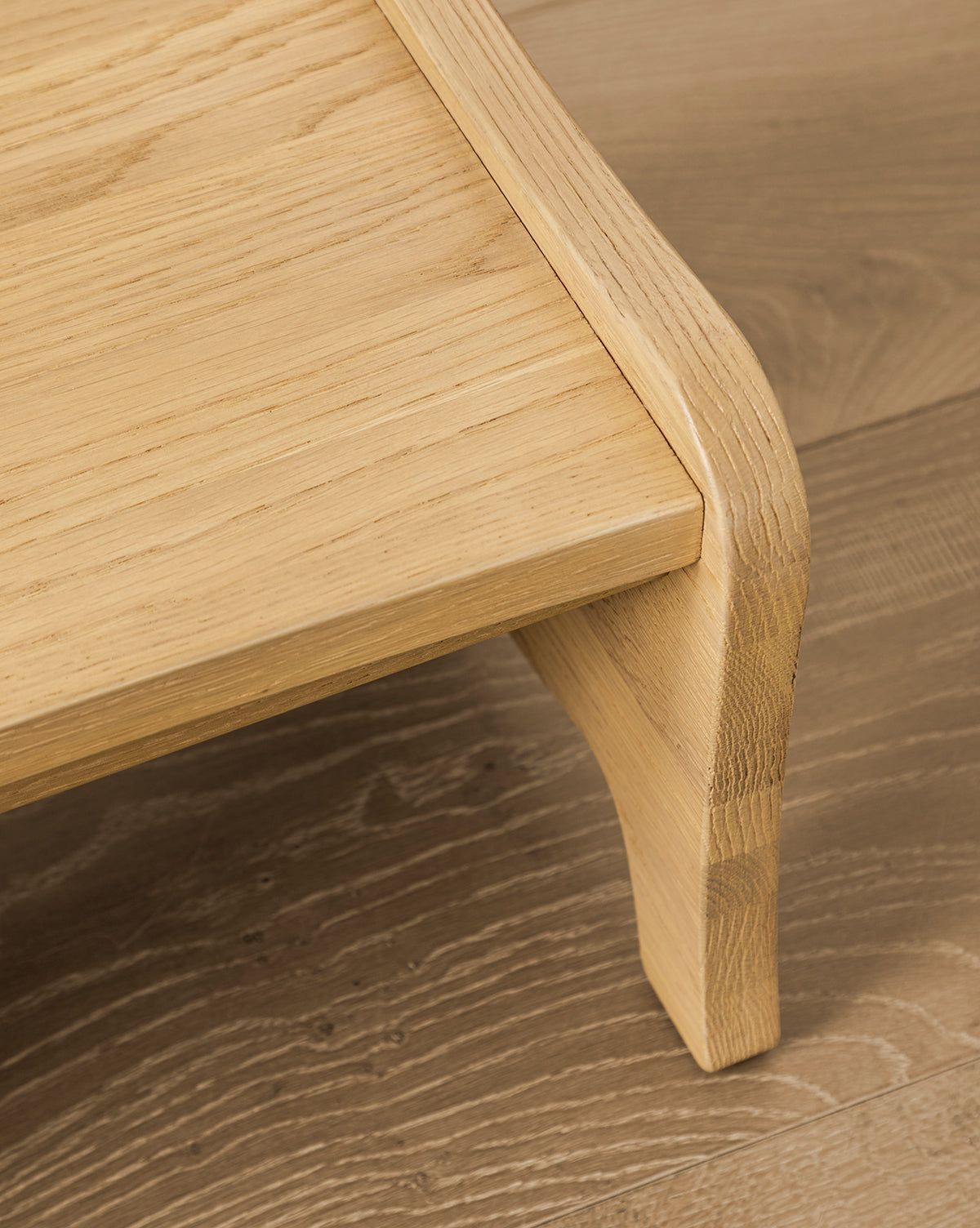 A close-up of the Gable Step Stool by YANG CHENG WOODEN INDUSTRIES INTERNATIONAL (VIETNAM) CO LTD shows its smooth, rounded edges and visible wood grain, placed on a wooden floor with a matching finish, reminiscent of the refined aesthetic often associated with McGee & Co.