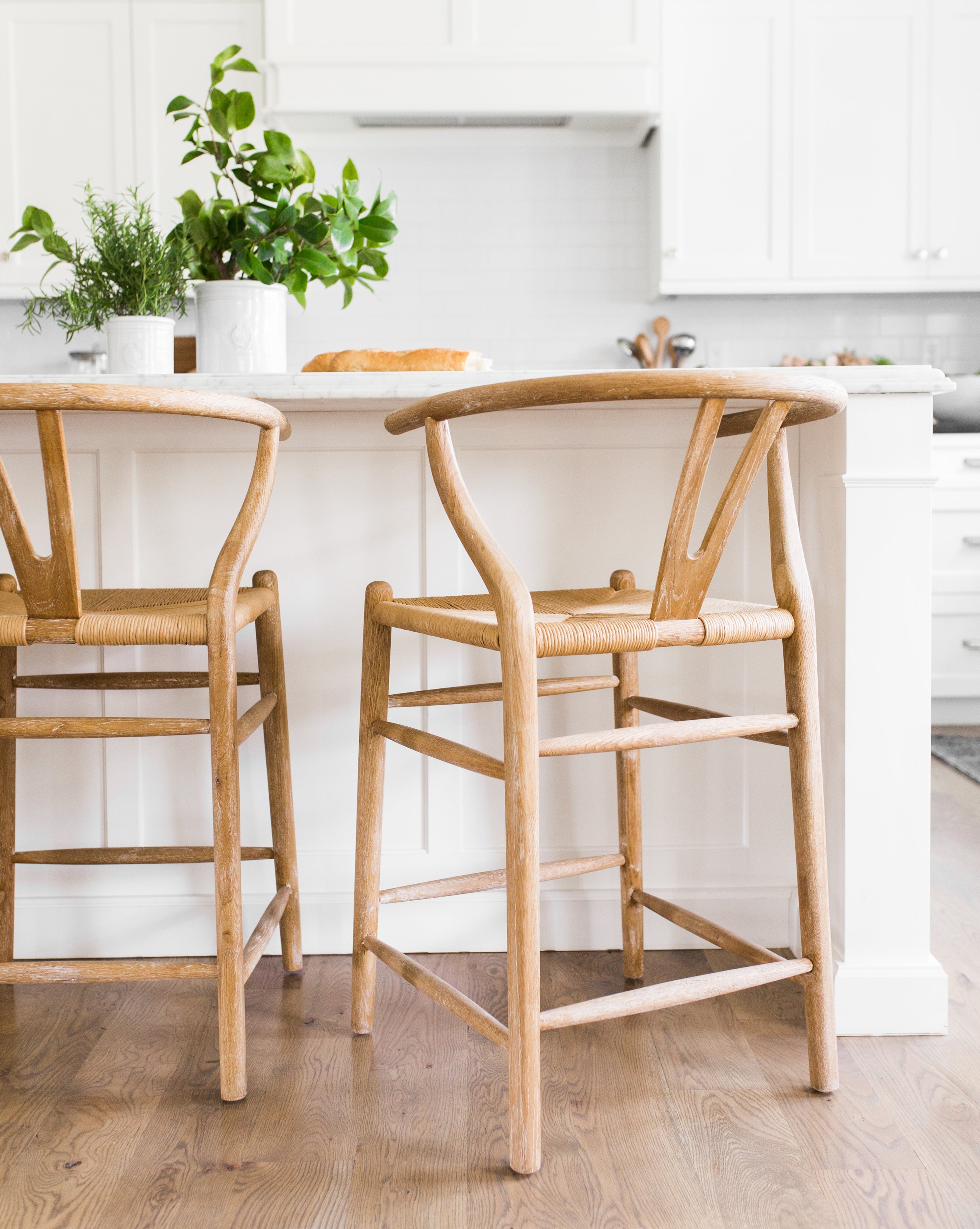 Two Gabriel Counter Stools with rope seats are positioned at a white kitchen island, by McGee & Co.